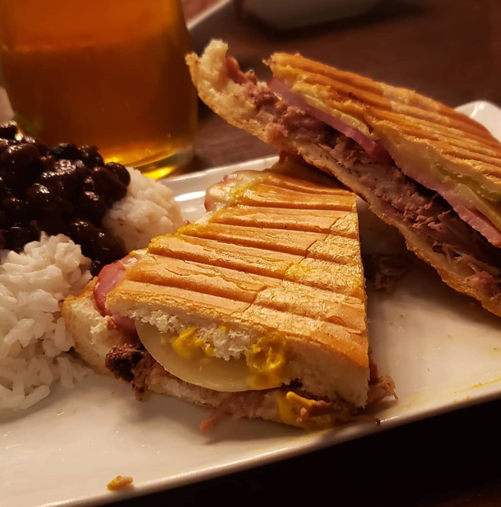 Cuban sandwich with rice, black beans, and drink on a plate.
