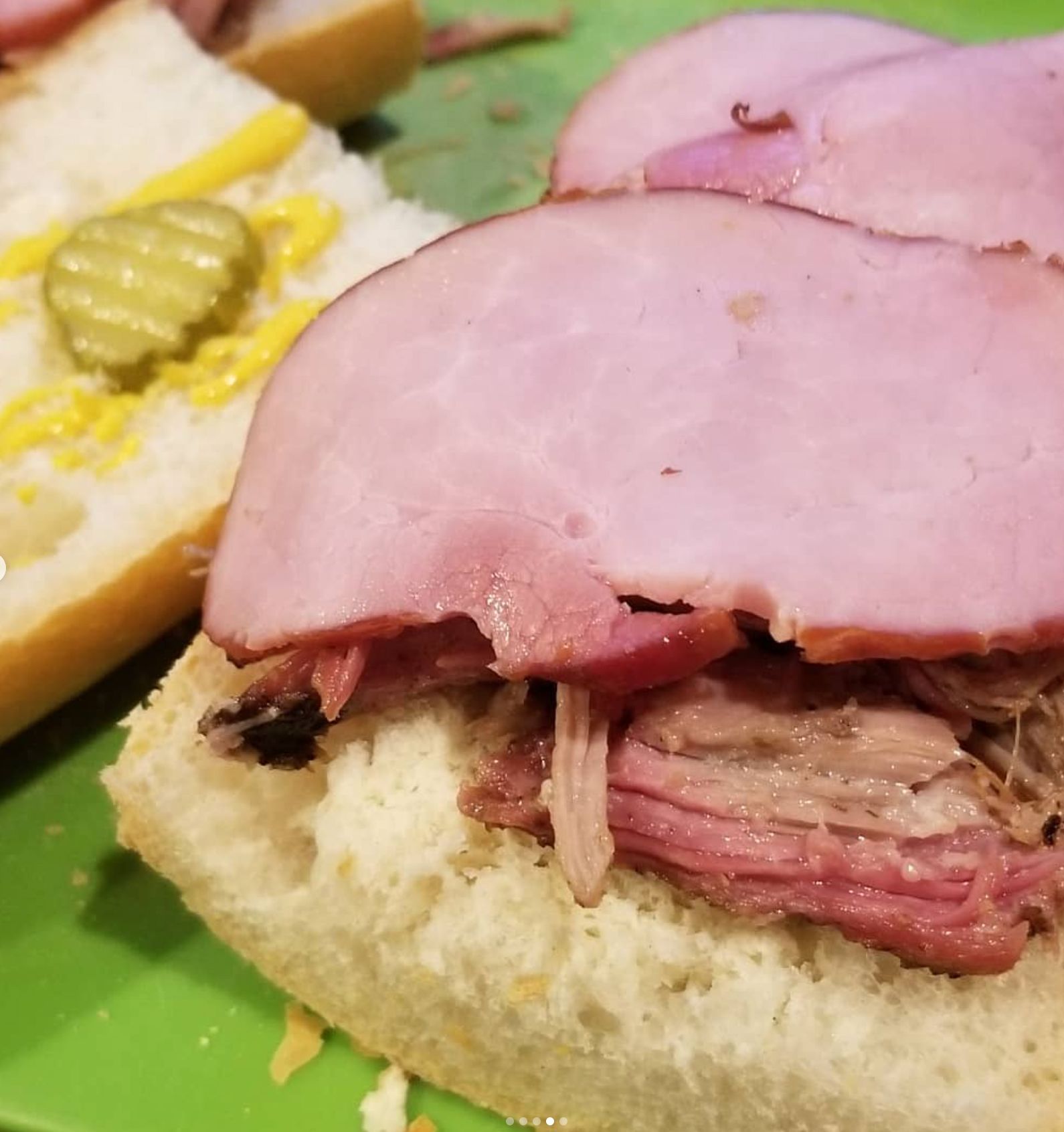 Ham and pulled pork sandwich on a bun with mustard and pickle.