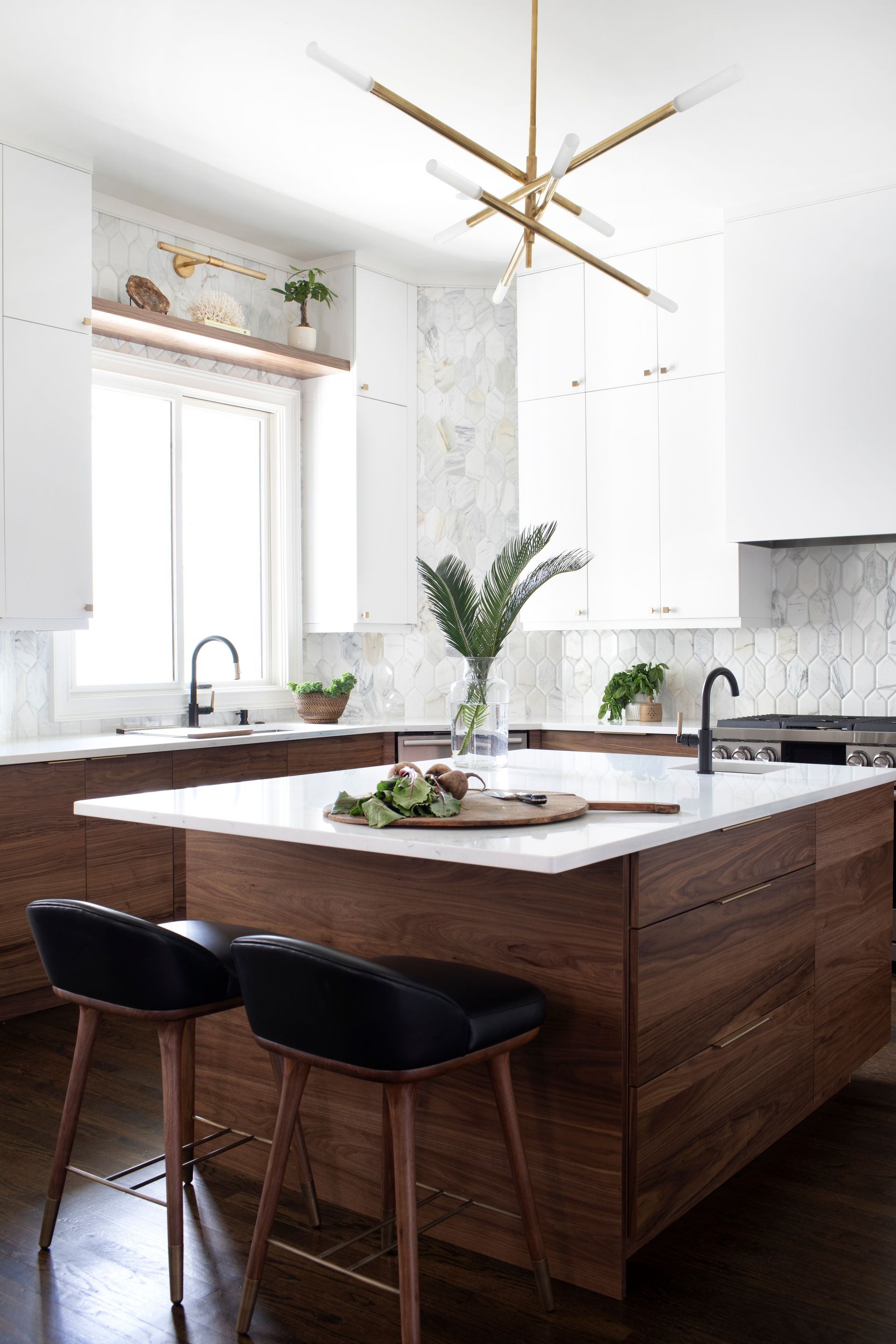 Modern kitchen with wood island, white countertops, and black stools. Overhead gold light fixture.