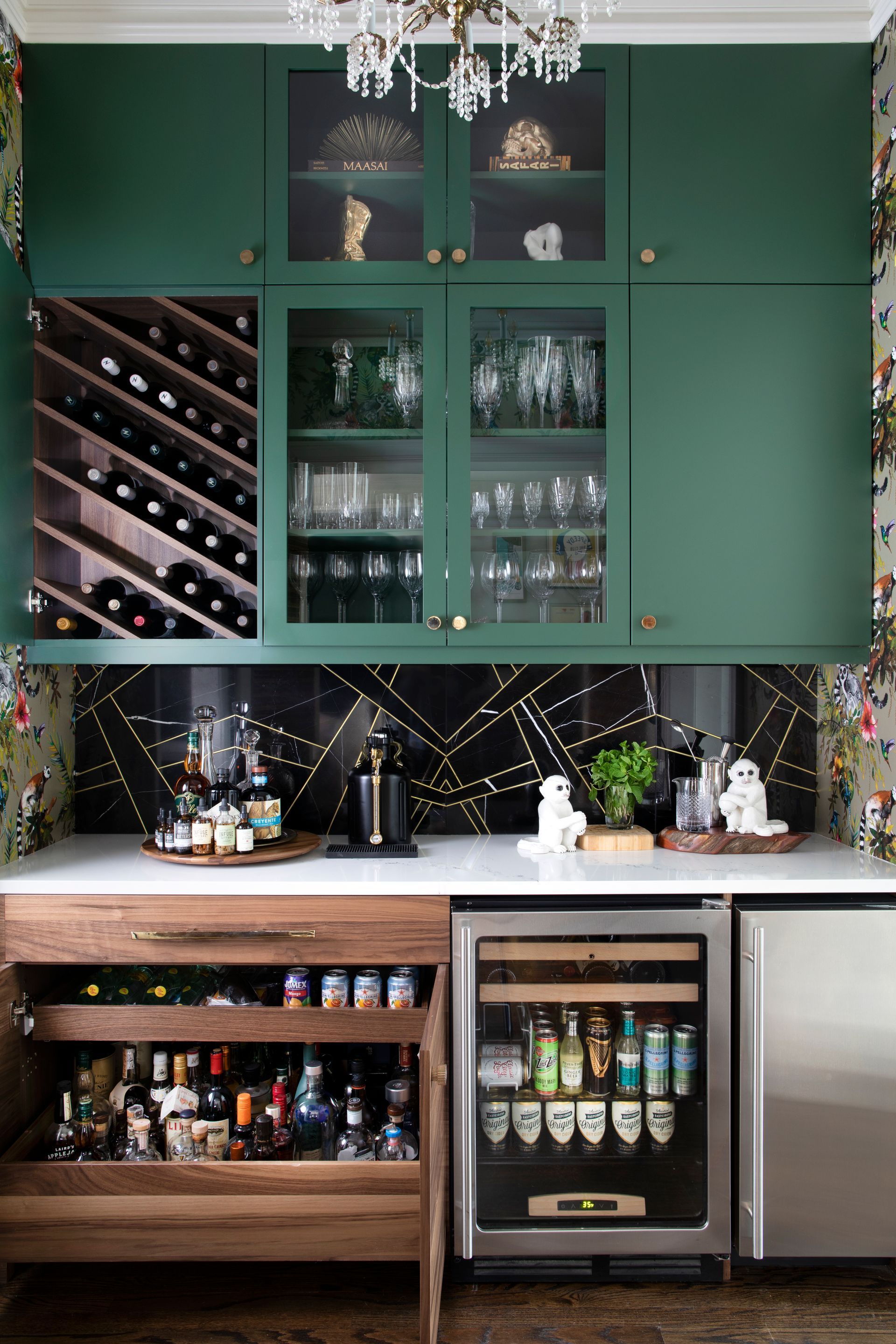 Green home bar with wine storage, glassware, and drinks. Wooden cabinet with drinks. White countertop.