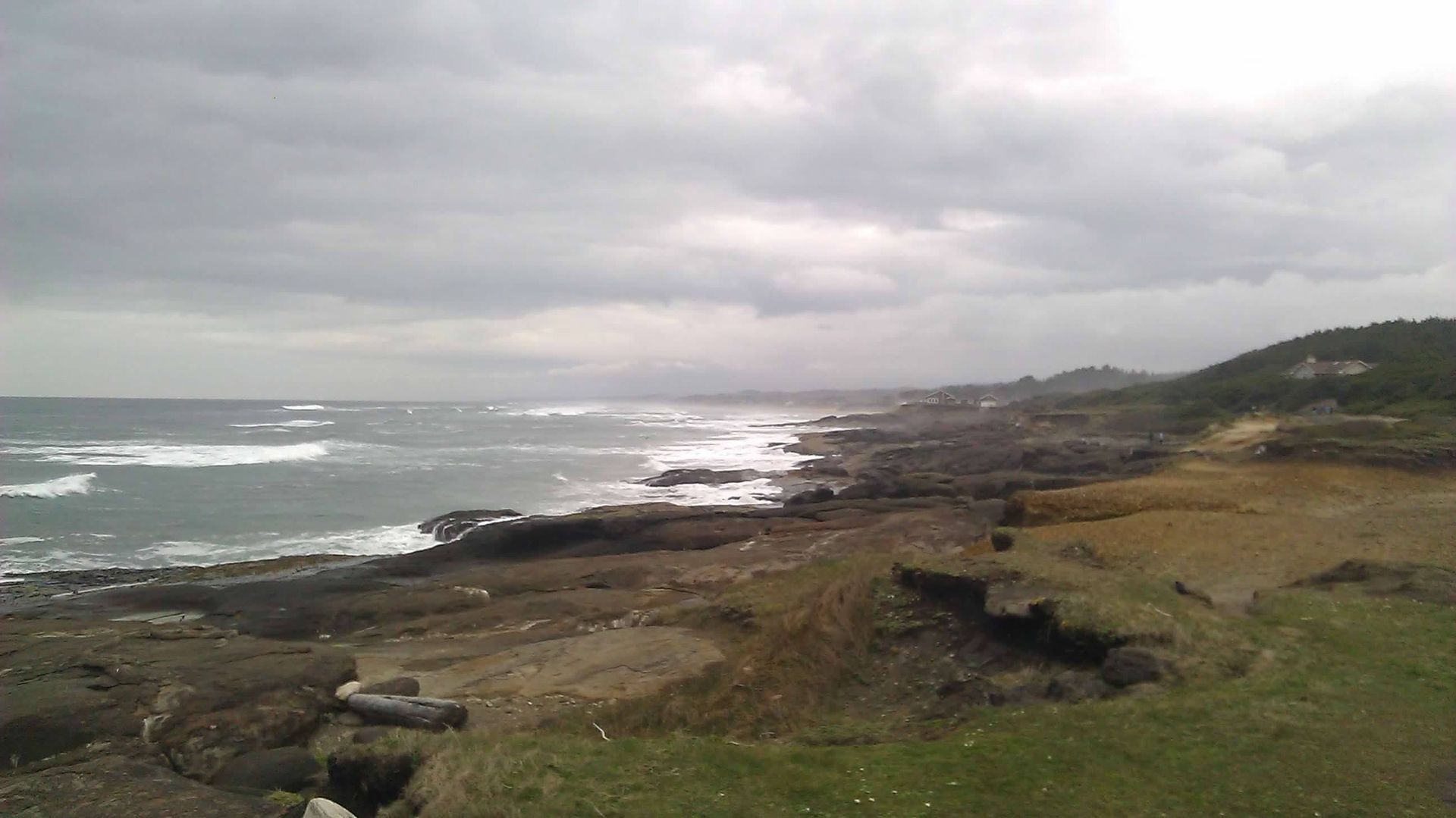 Rocky coastline under an overcast sky. Choppy waves crash against the shore.