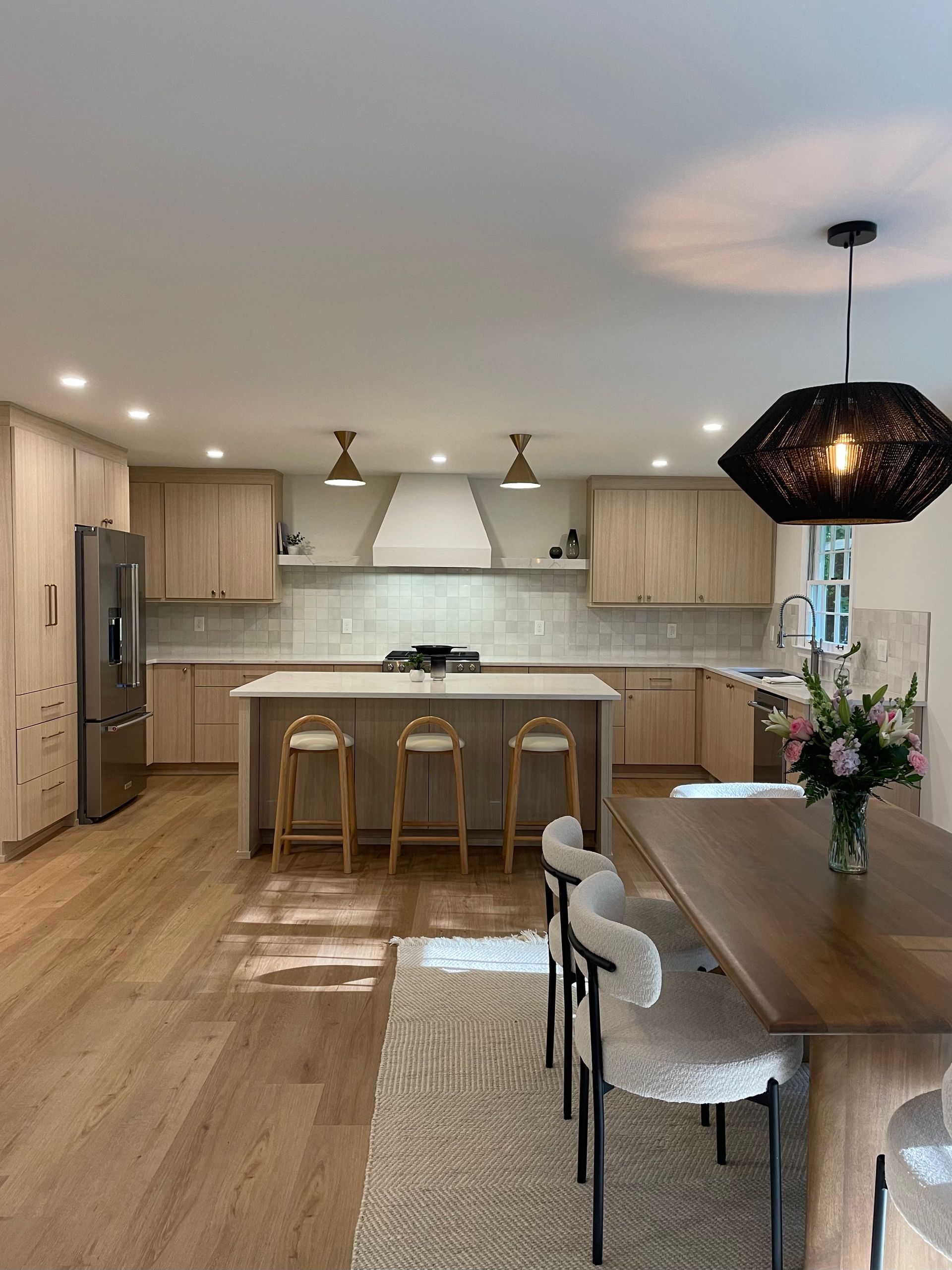 Spacious kitchen with wood cabinets, island, and dining area. Neutral colors with modern pendant lights and wood floors.