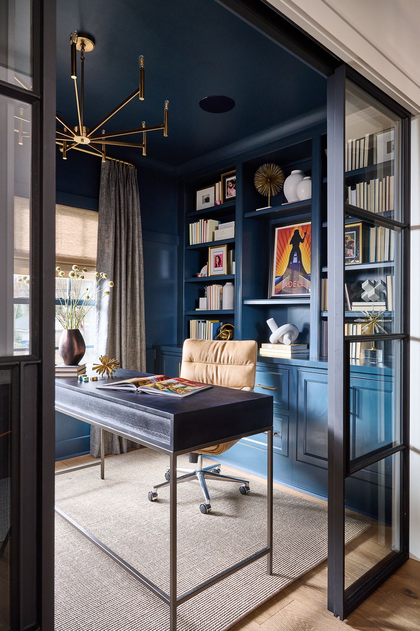 Blue home office with glass door, desk, shelves with books, and a patterned rug.