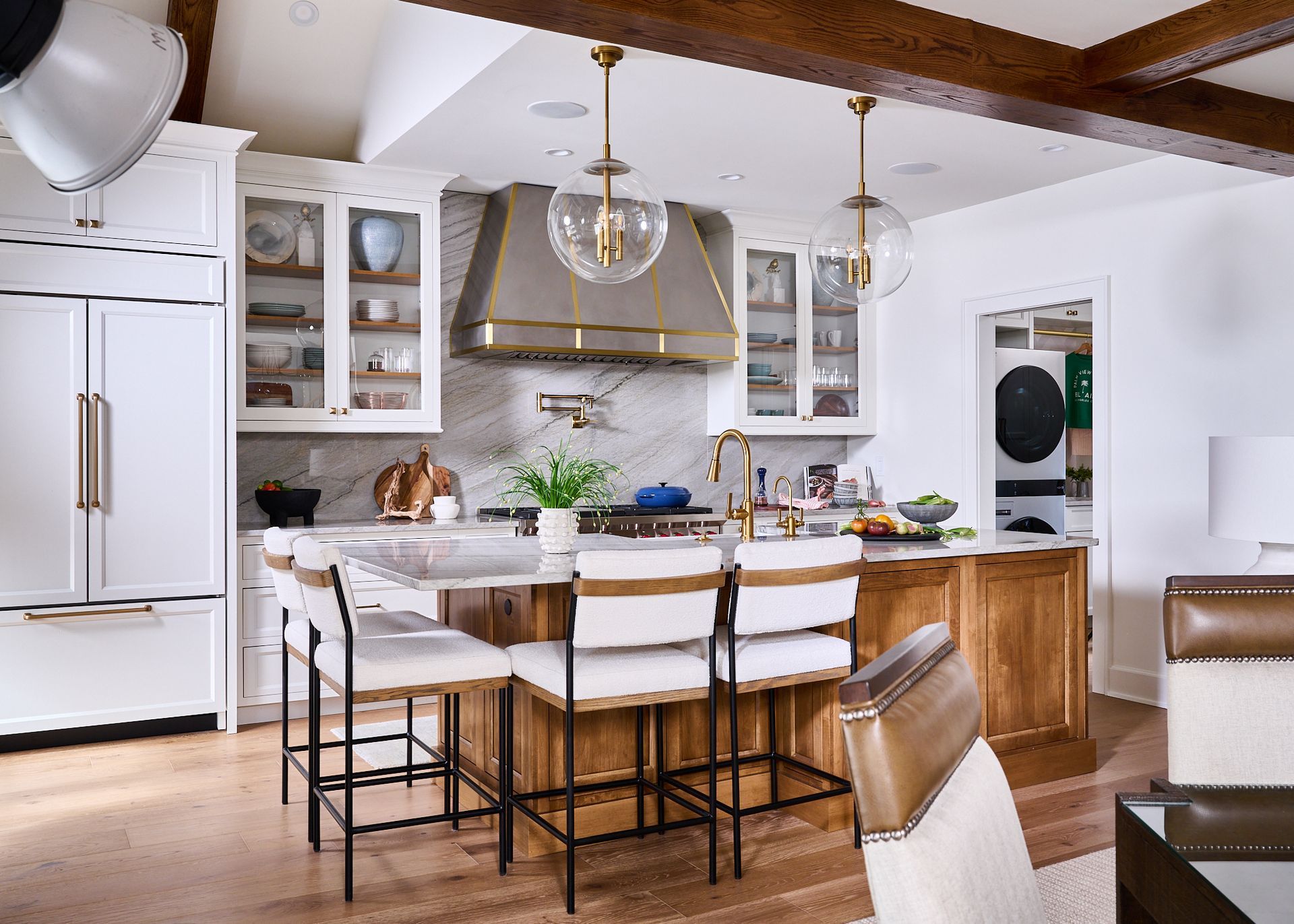 Kitchen with a large island, white cabinets, marble backsplash, and gold accents.