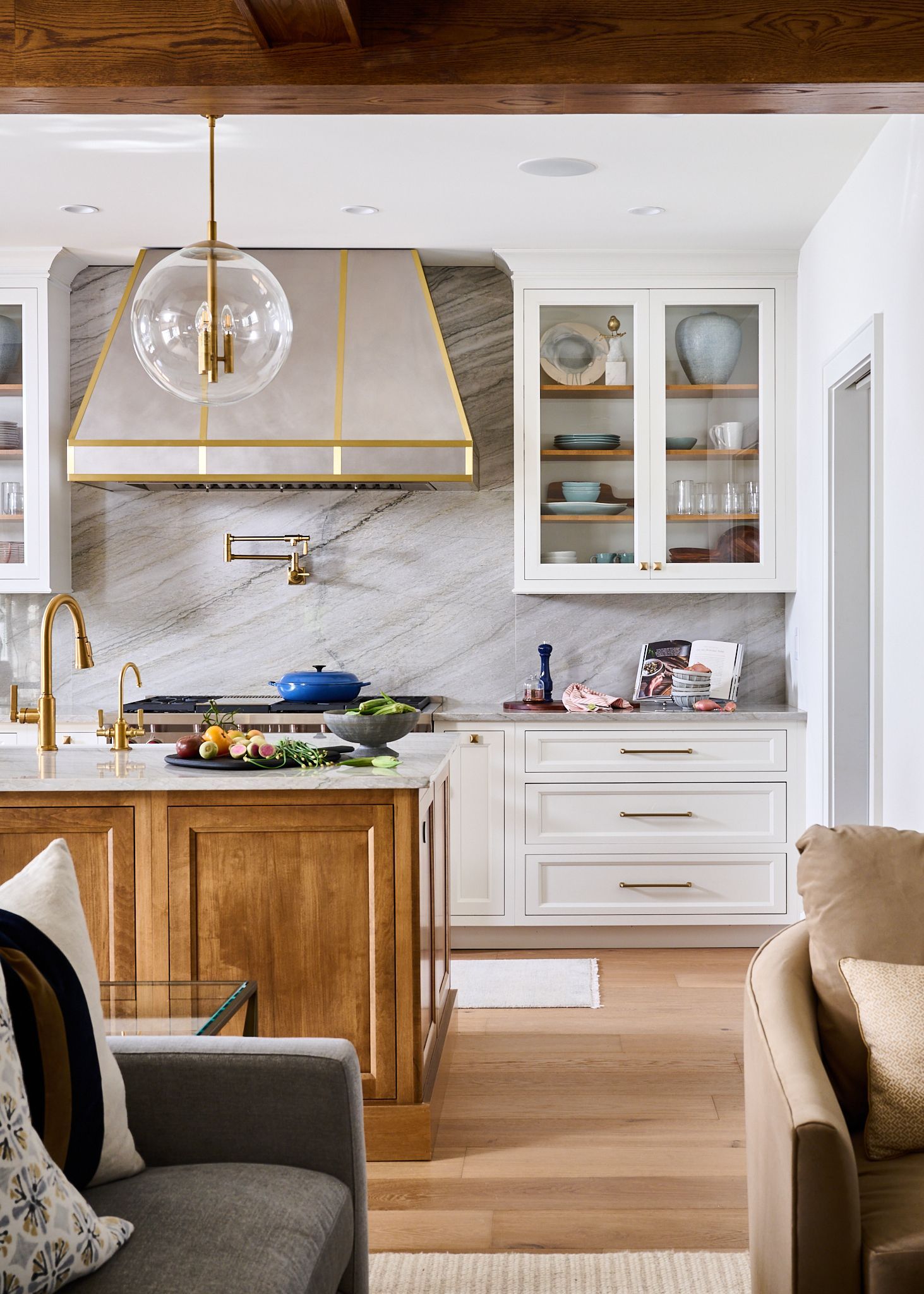Elegant kitchen with wooden island, white cabinets, gold accents, and a marble backsplash.