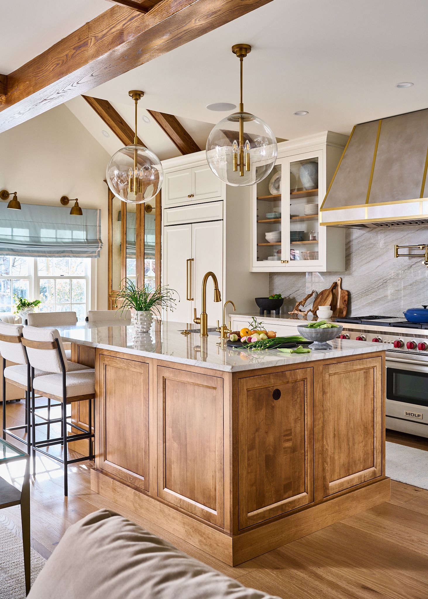 Elegant kitchen with wood island, marble countertops, glass globe pendants, and a large range.