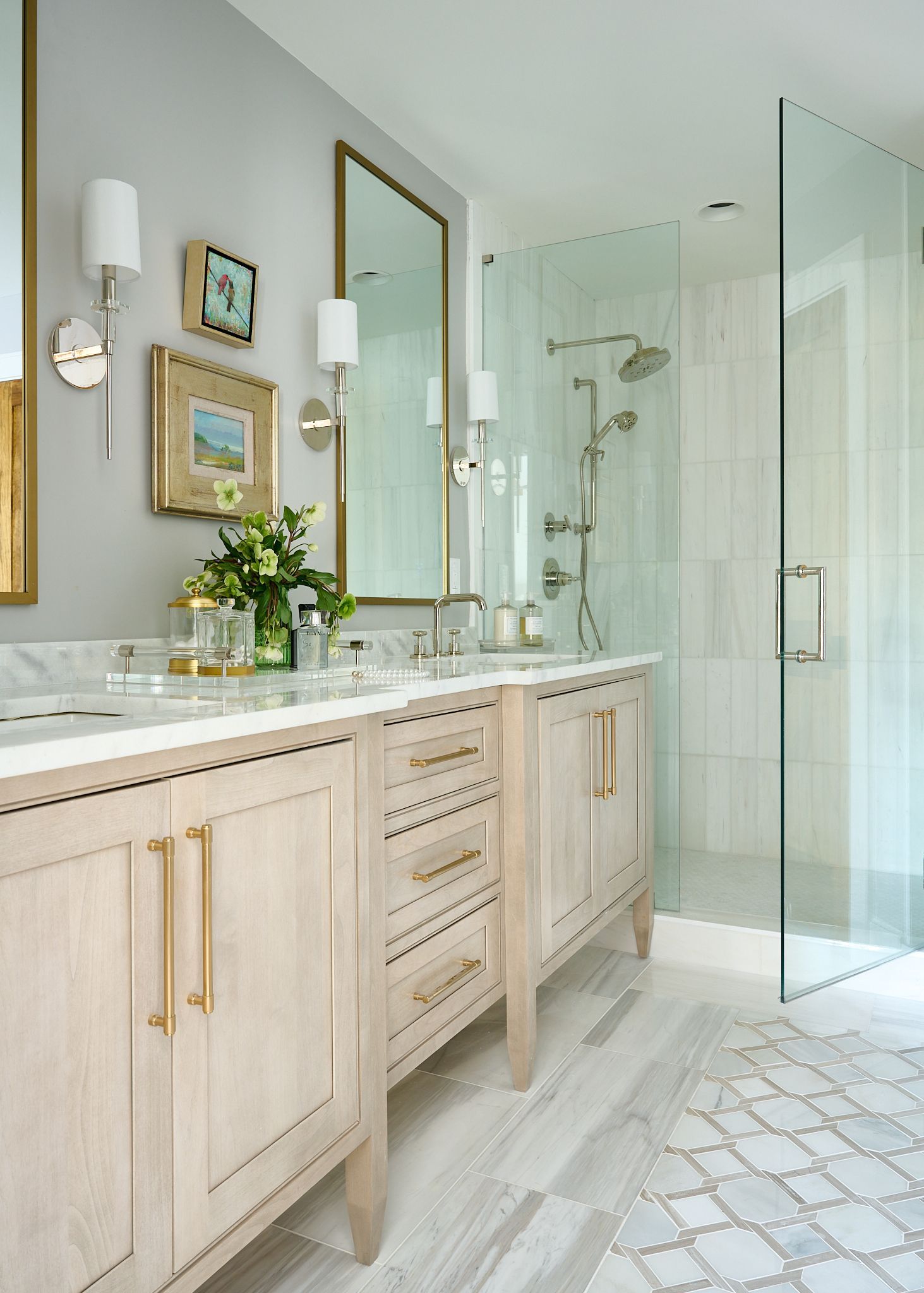 Elegant bathroom with light wood double vanity, gold hardware, and glass shower.