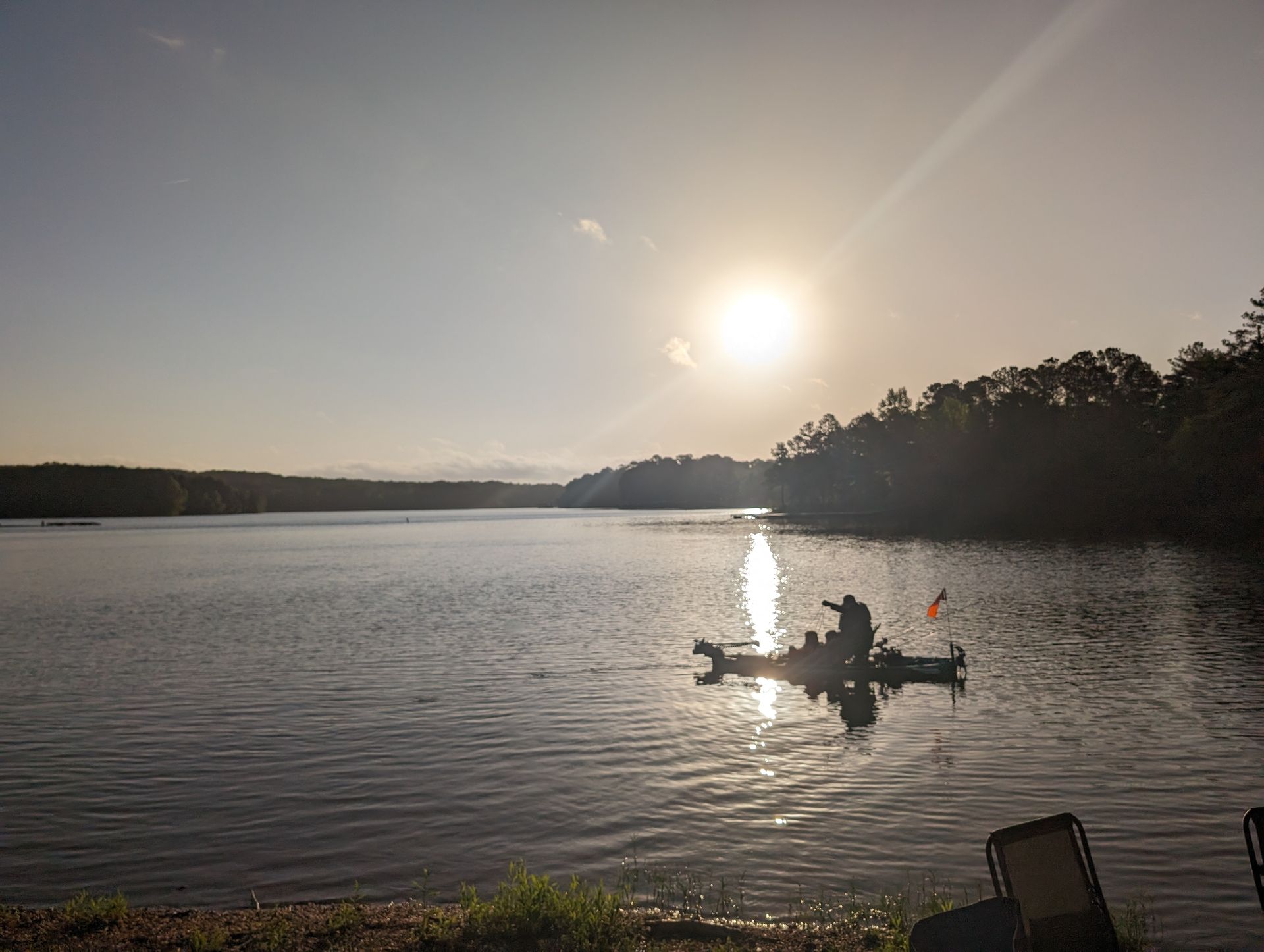 Kayaker on a lake at sunrise; trees line the shore.