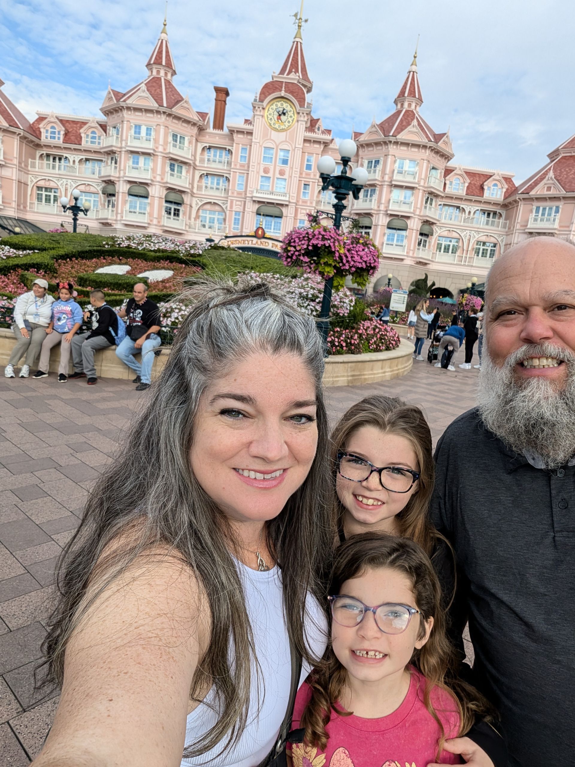 Family selfie at a pink Disneyland castle with two children. Everyone smiles.