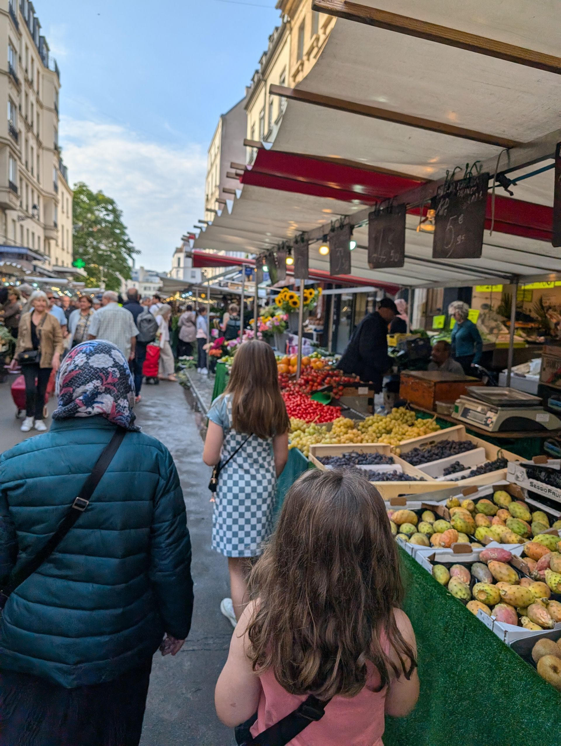 Market street scene with people and stalls of produce under awnings.