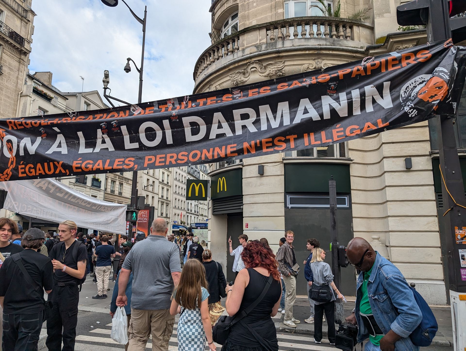 Protest with banner against the Darmanin law in front of a McDonald's in a city street.
