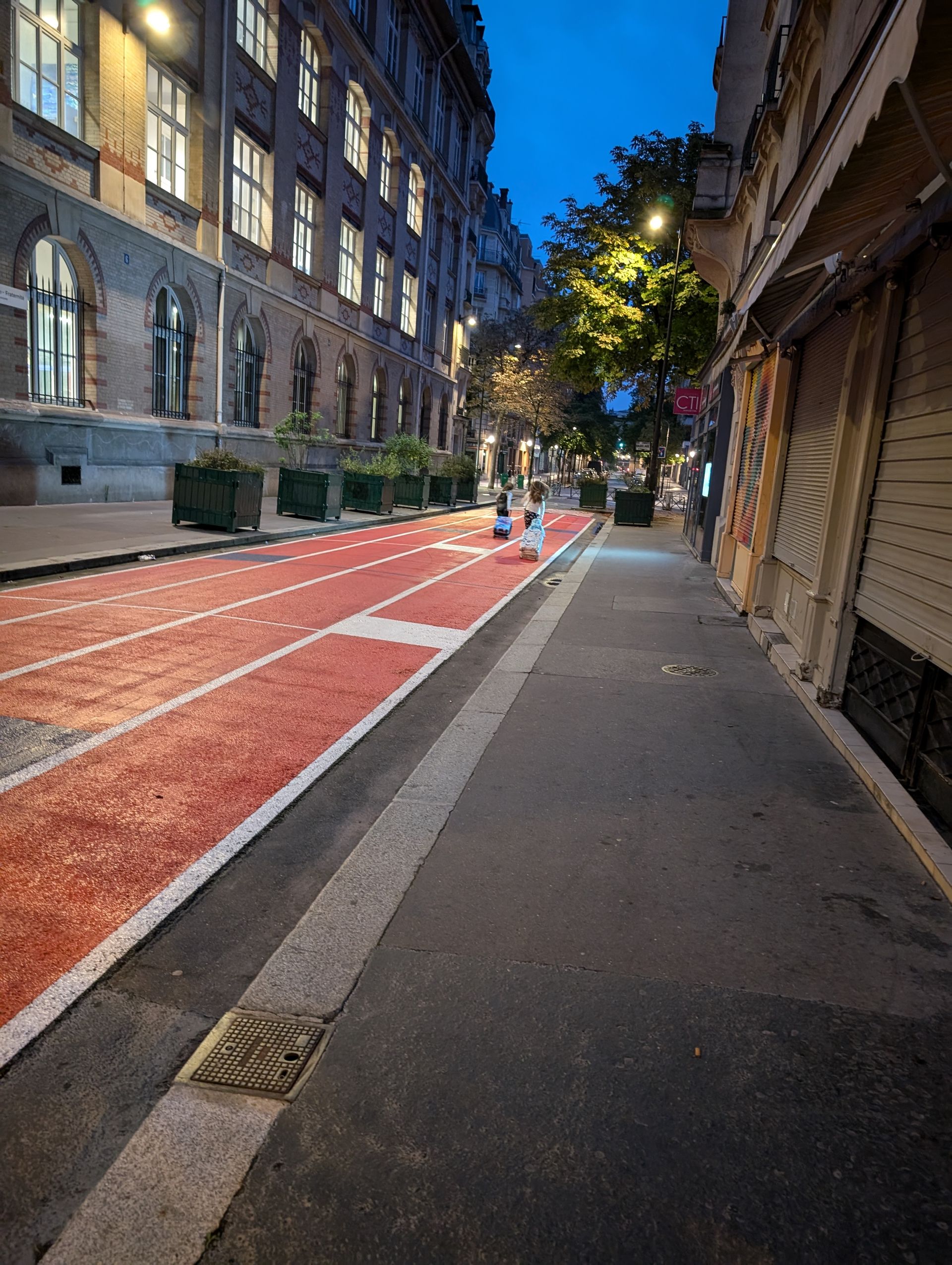 A red bike lane with white lines on a street in an urban setting at dusk. Buildings line the street.