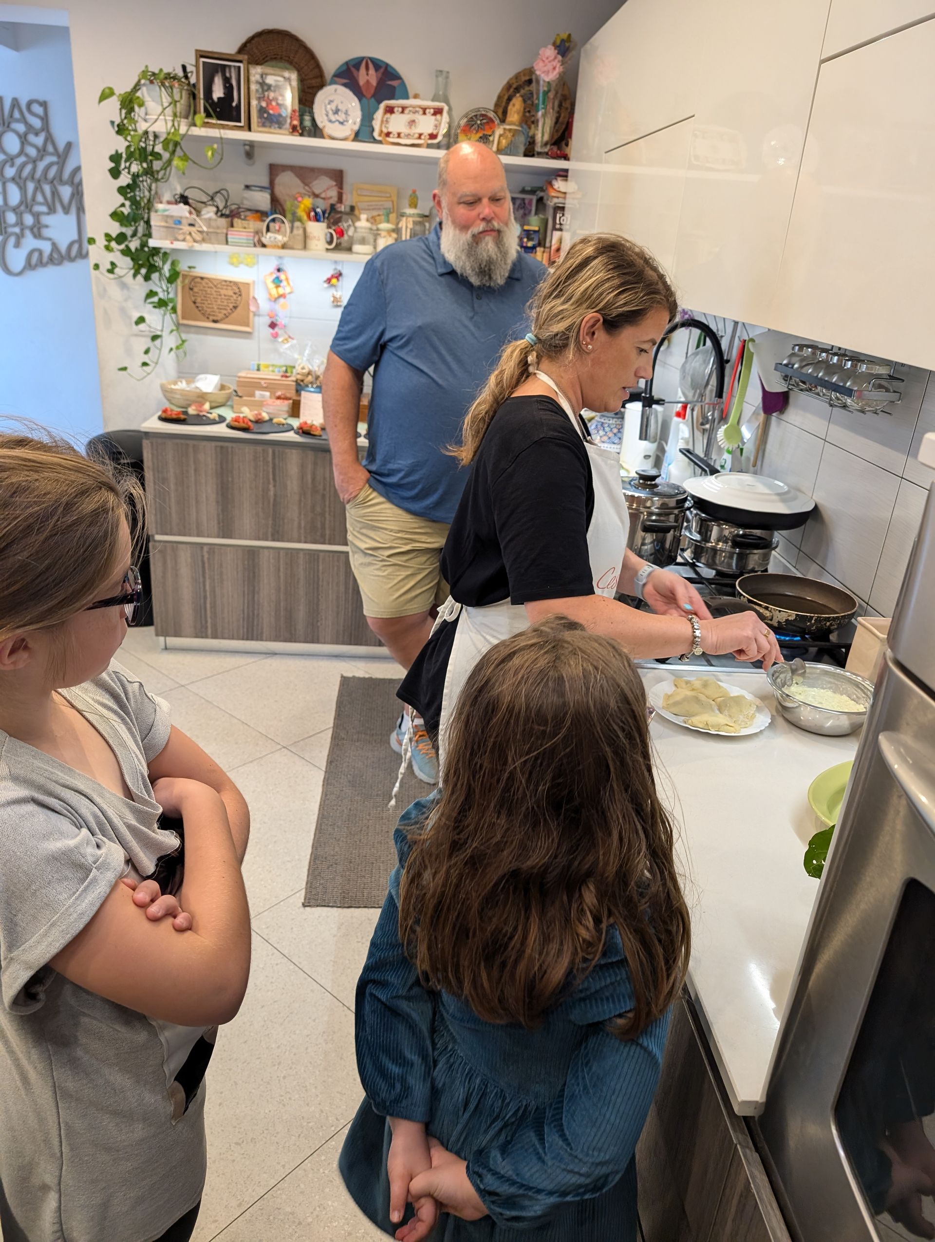 Woman cooking with two children in kitchen; man watches.