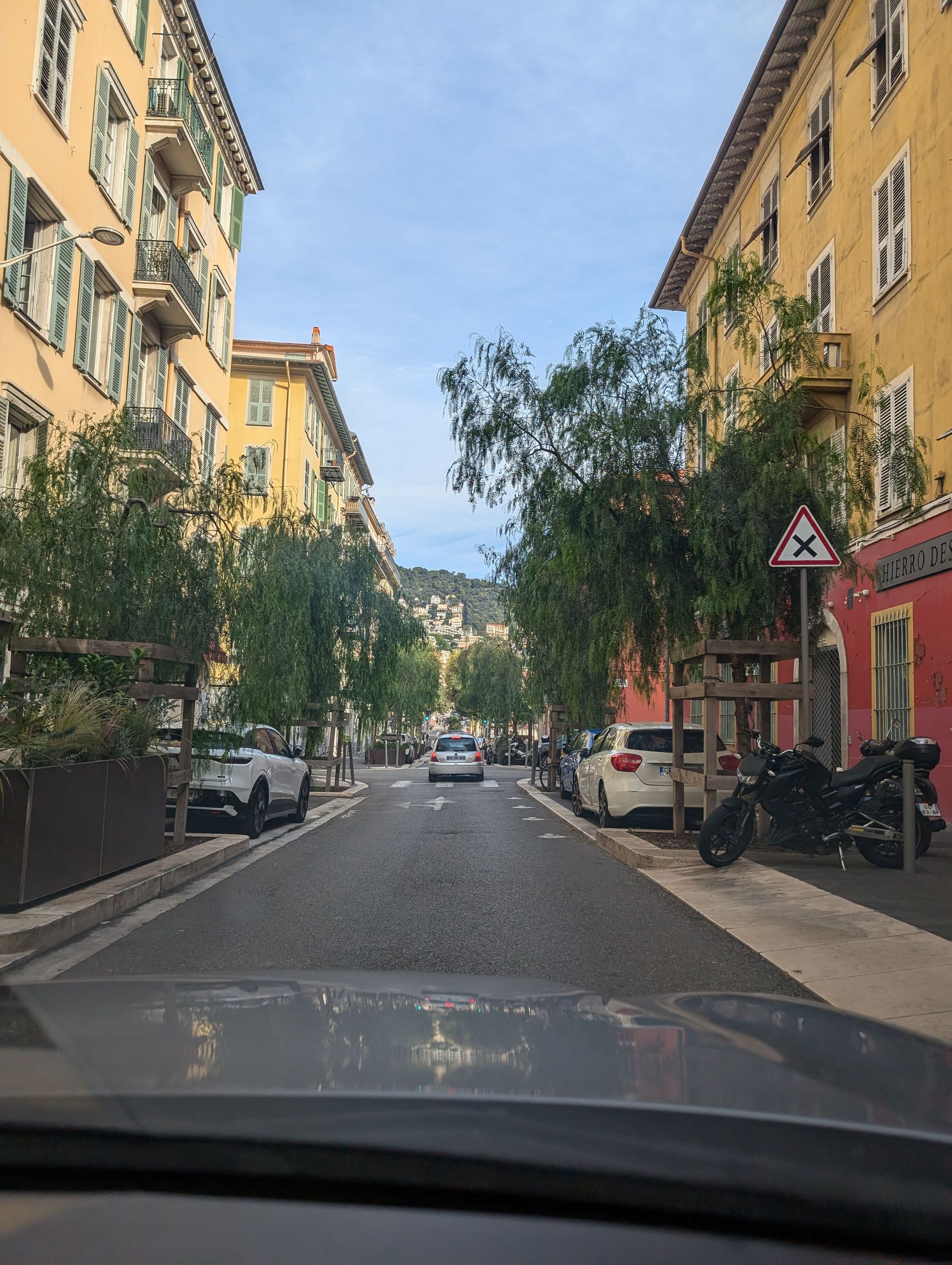 Narrow street lined with yellow buildings and trees in Nice, France.