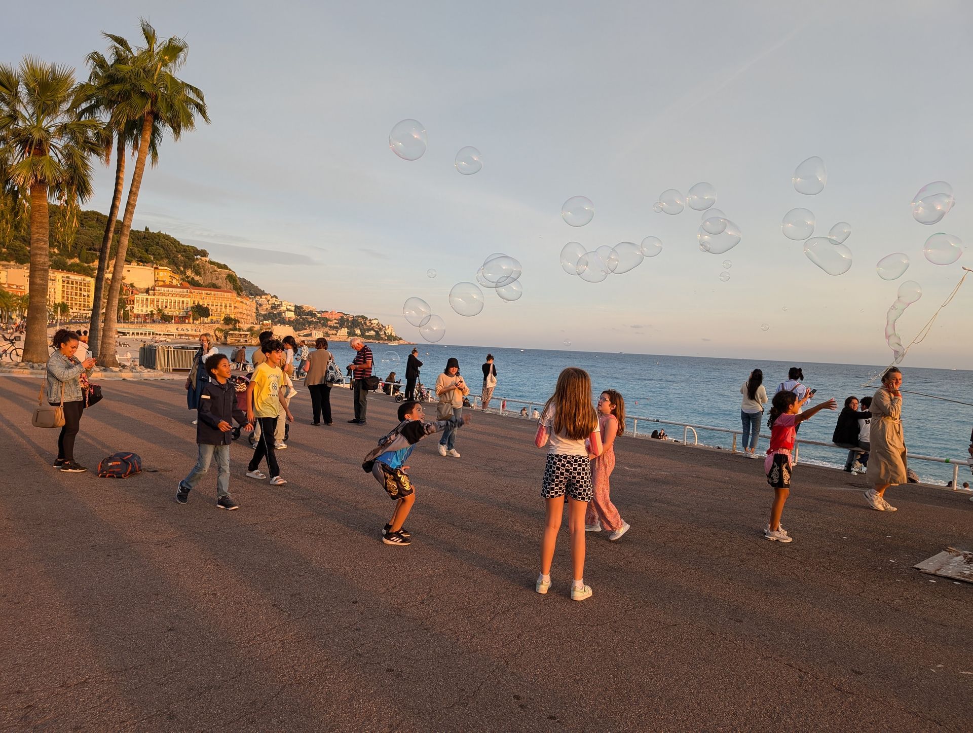 Children playing with bubbles on a beach; palm trees, ocean, and hillside in the background.