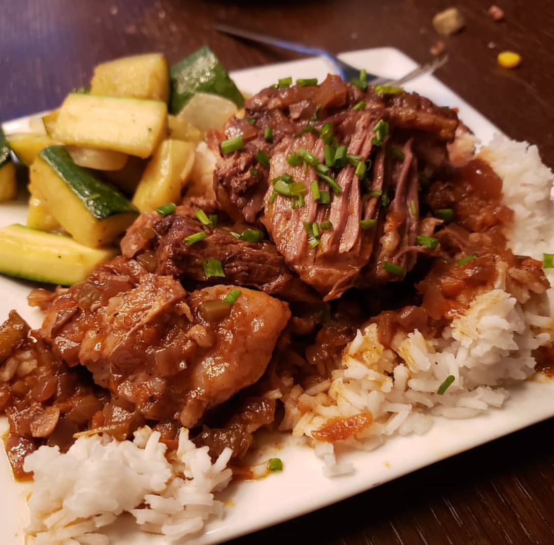 Plate of braised meat with rice, zucchini, and garnished with chives.