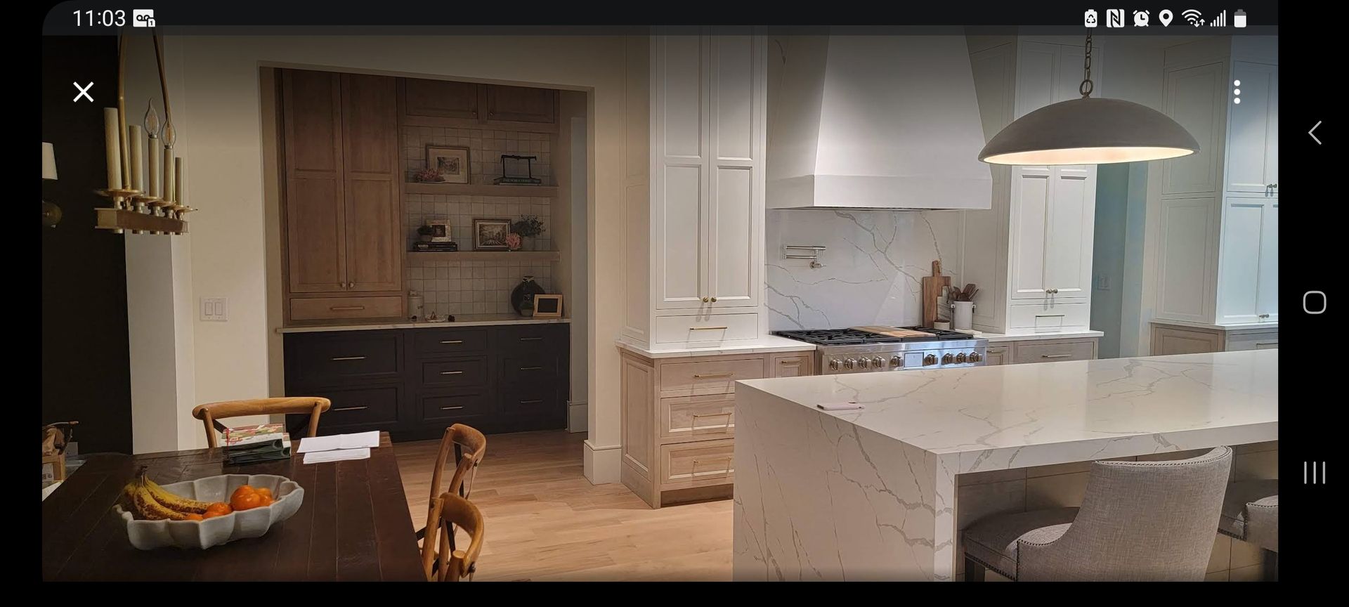 Kitchen with white island, cabinets, and appliances. A dark wood dining table is in the foreground.