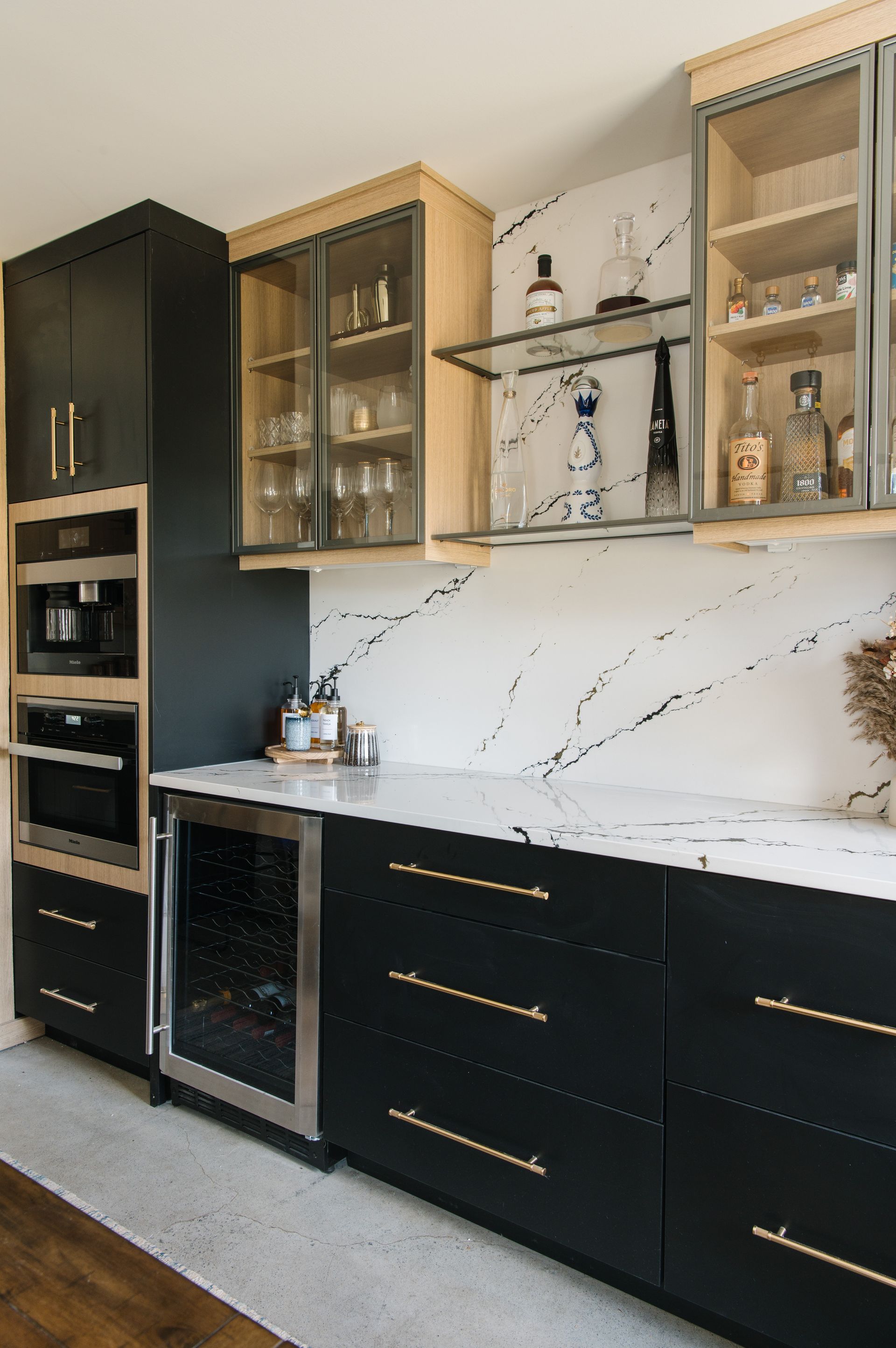 Black and wood-tone kitchen with marble backsplash. Built-in appliances, cabinets, and a wine fridge.