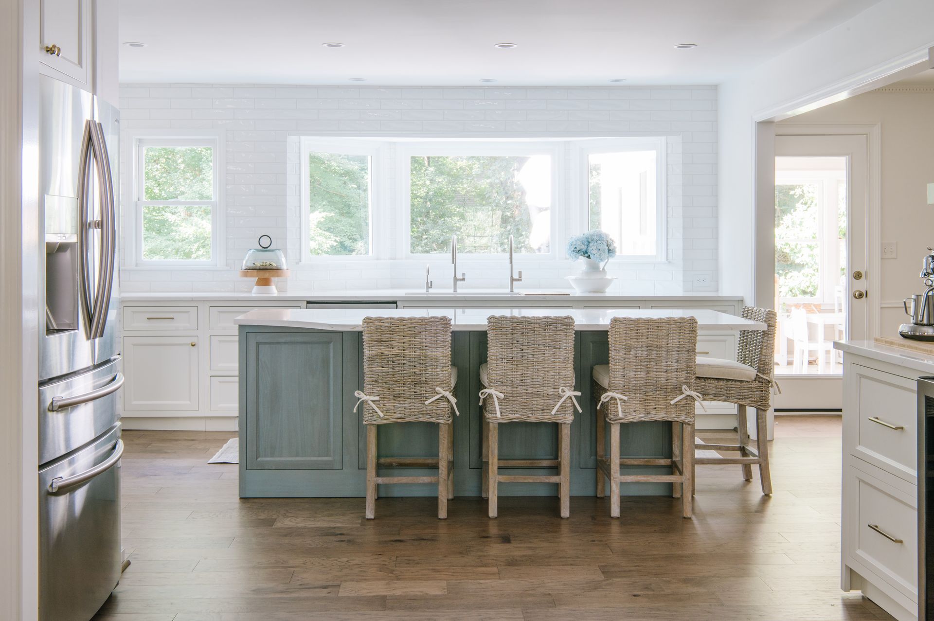 Spacious kitchen with blue island, white cabinets, and wooden floors. Three barstools face the island.