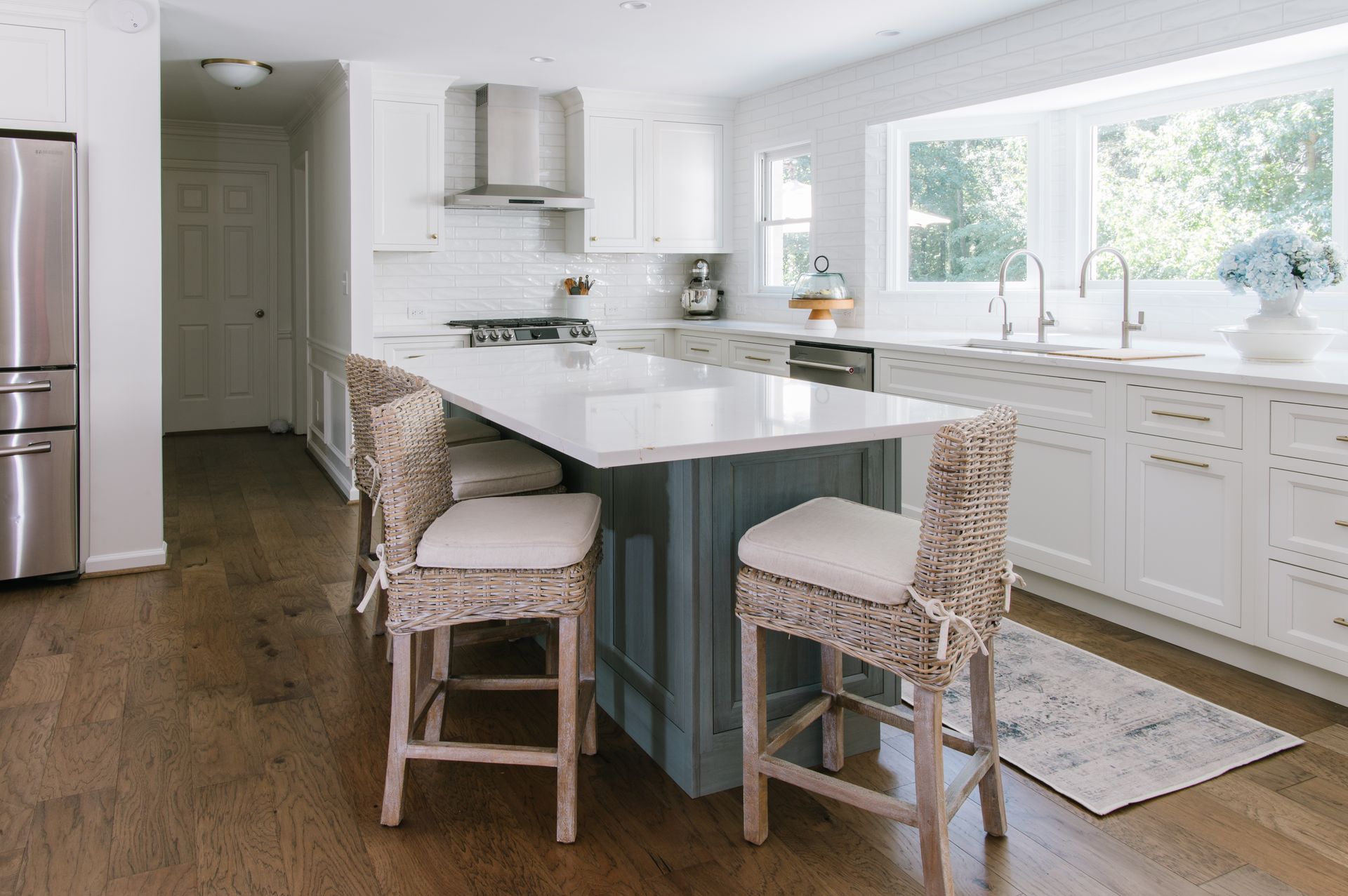Kitchen with white cabinets, blue island, wooden floor, and woven bar stools.