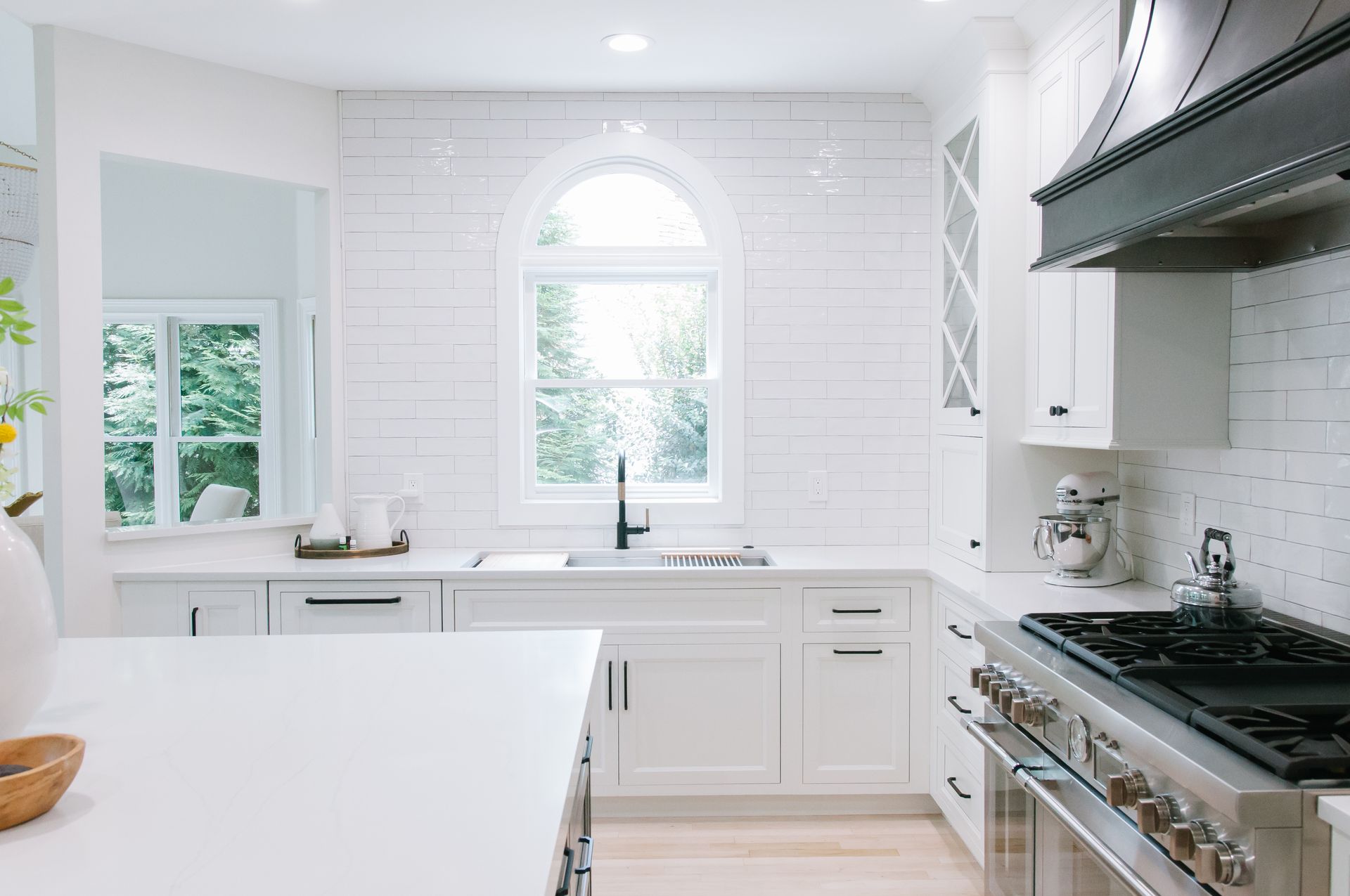 White kitchen with arched window, light wood floors, stainless steel appliances, and island.