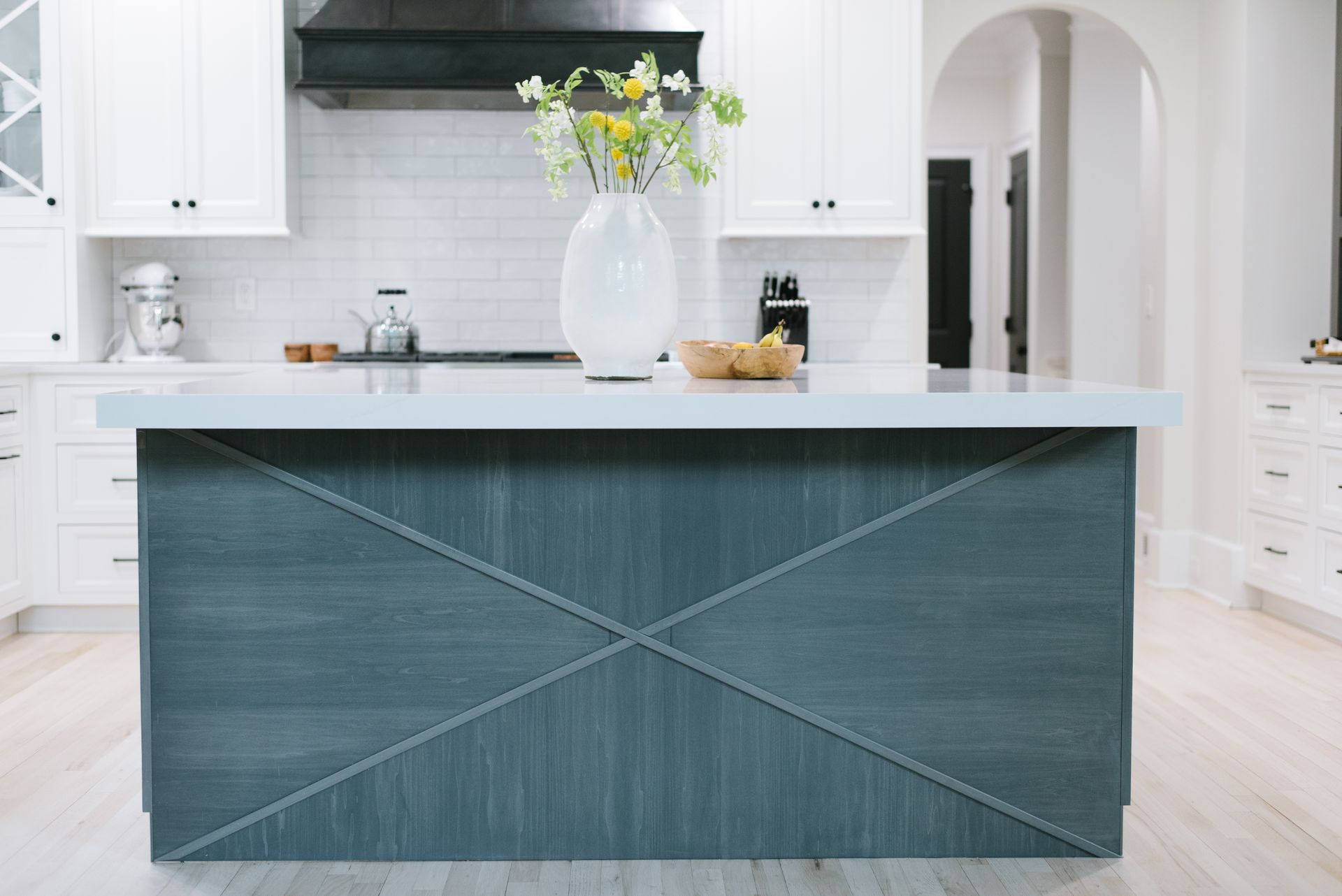 Kitchen island with gray-blue textured panels and white countertop. White cabinets and a black range hood.