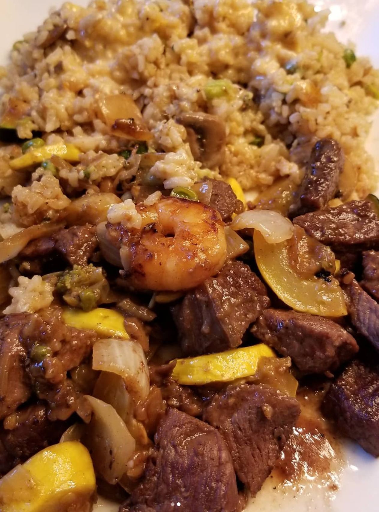 Hibachi-style meal with beef, shrimp, fried rice, squash, and onions on a white plate.