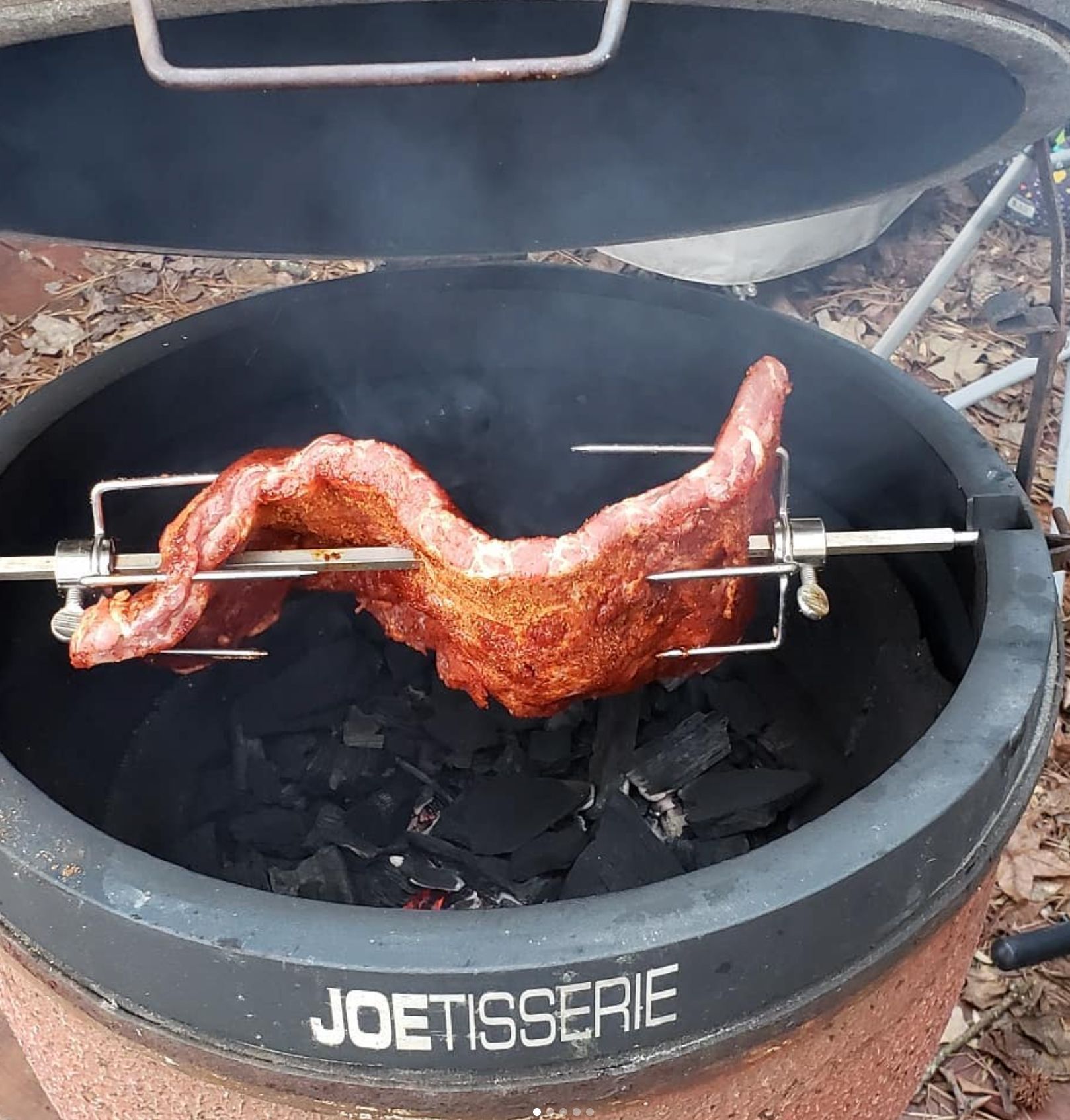 Ribs roasting on a rotisserie inside a JoeTisserie smoker with hot coals.