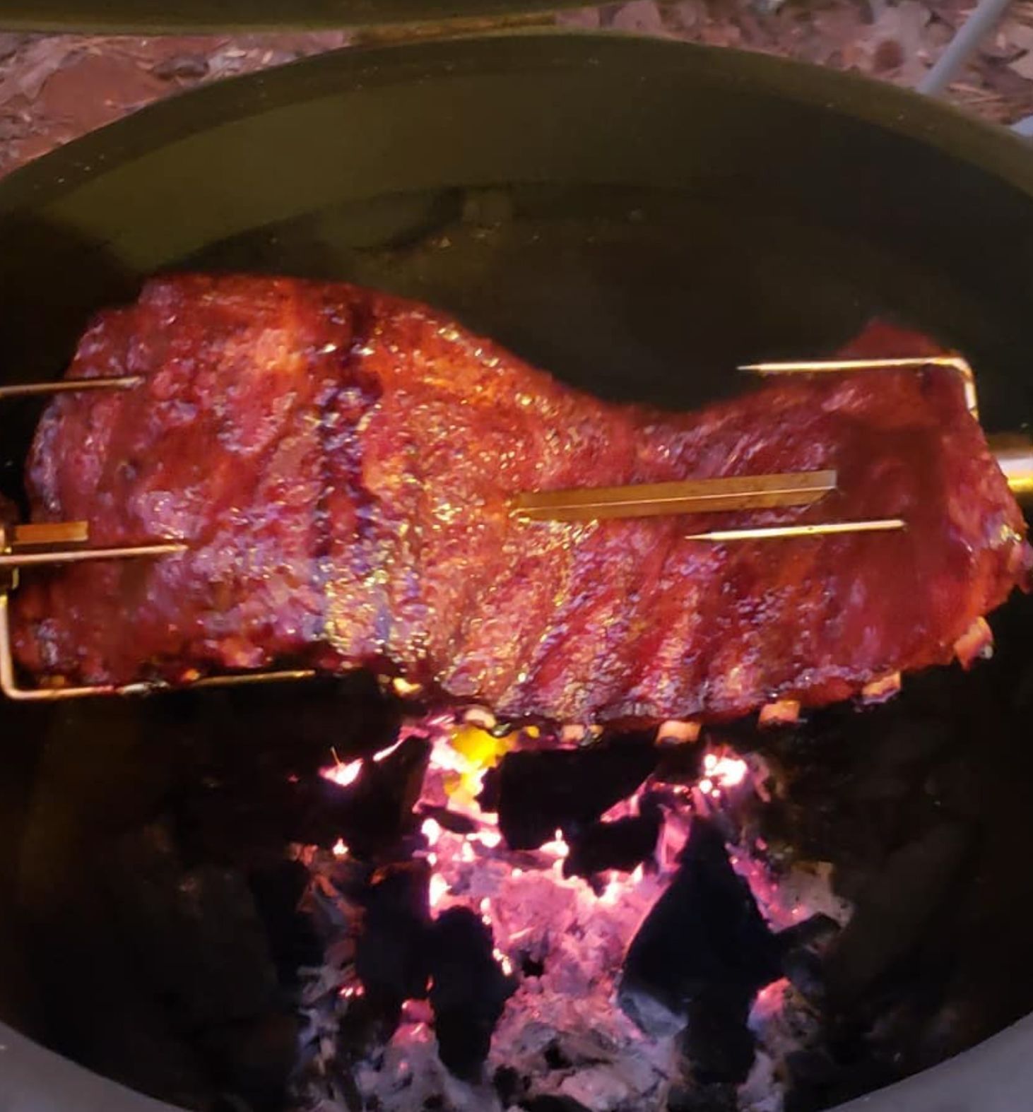 Rack of ribs on a rotisserie over glowing embers in a smoker.