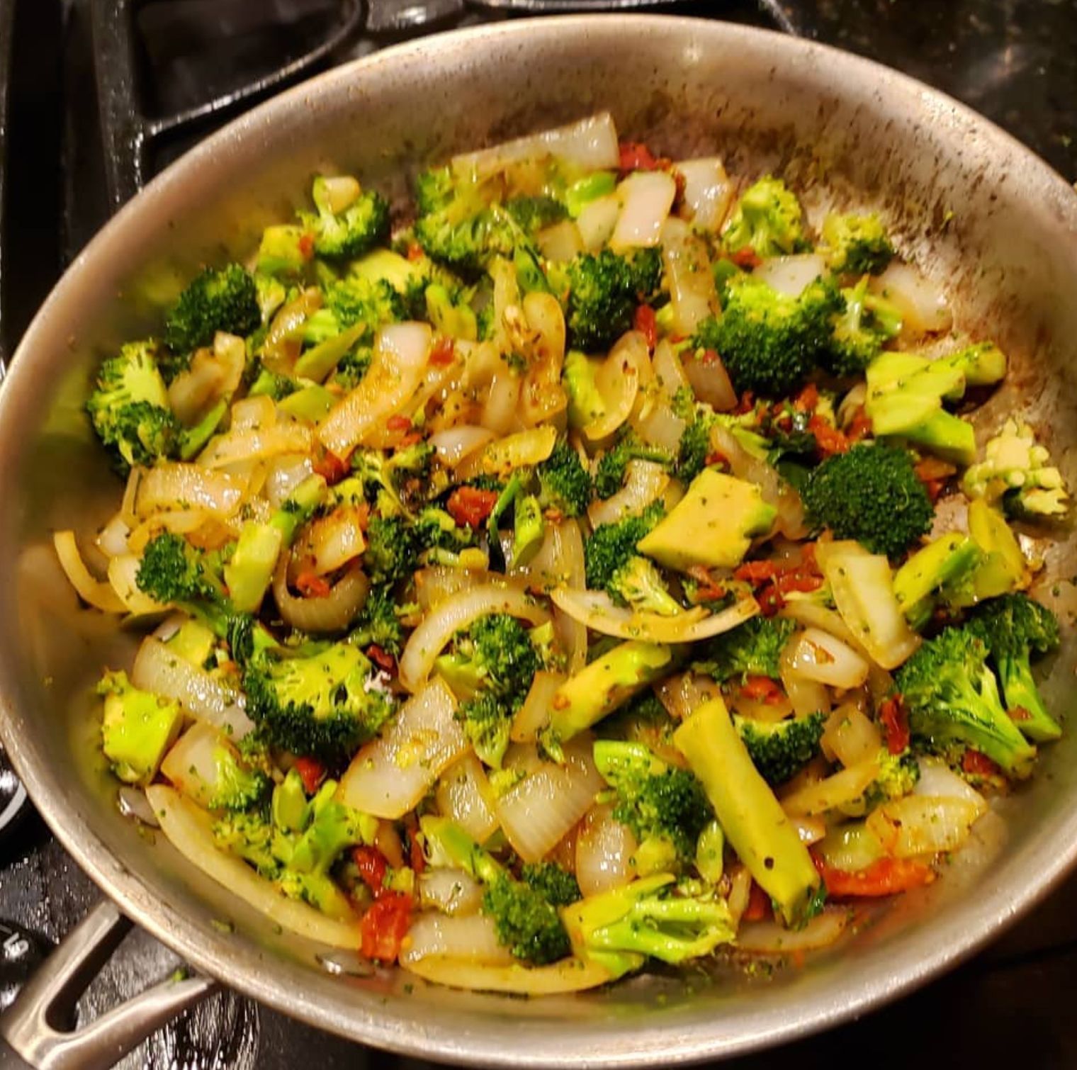 Broccoli and onions sautéing in a stainless steel pan on a stovetop, with seasonings.