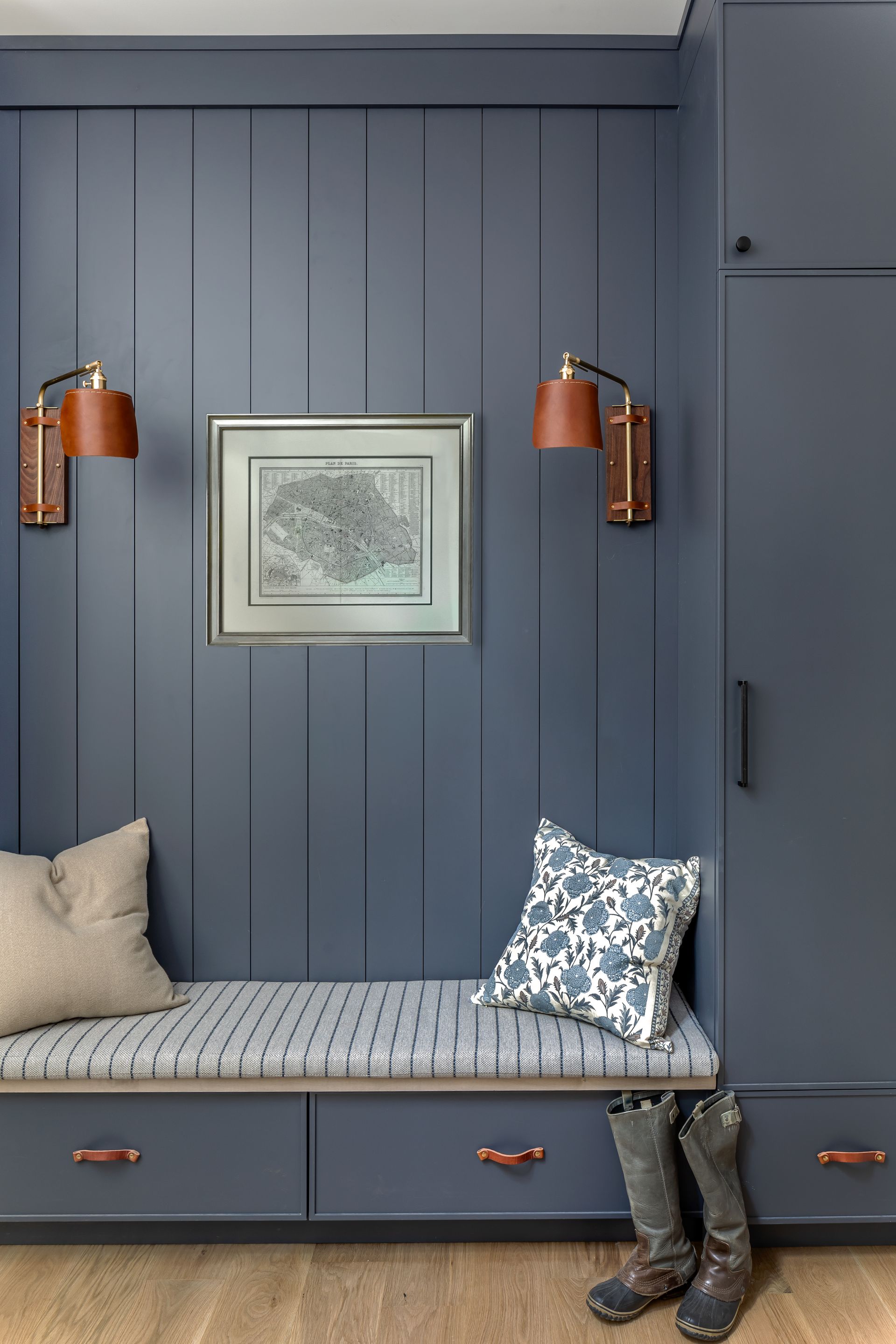 Navy blue entryway with built-in bench, storage drawers, leather sconces, and artwork.