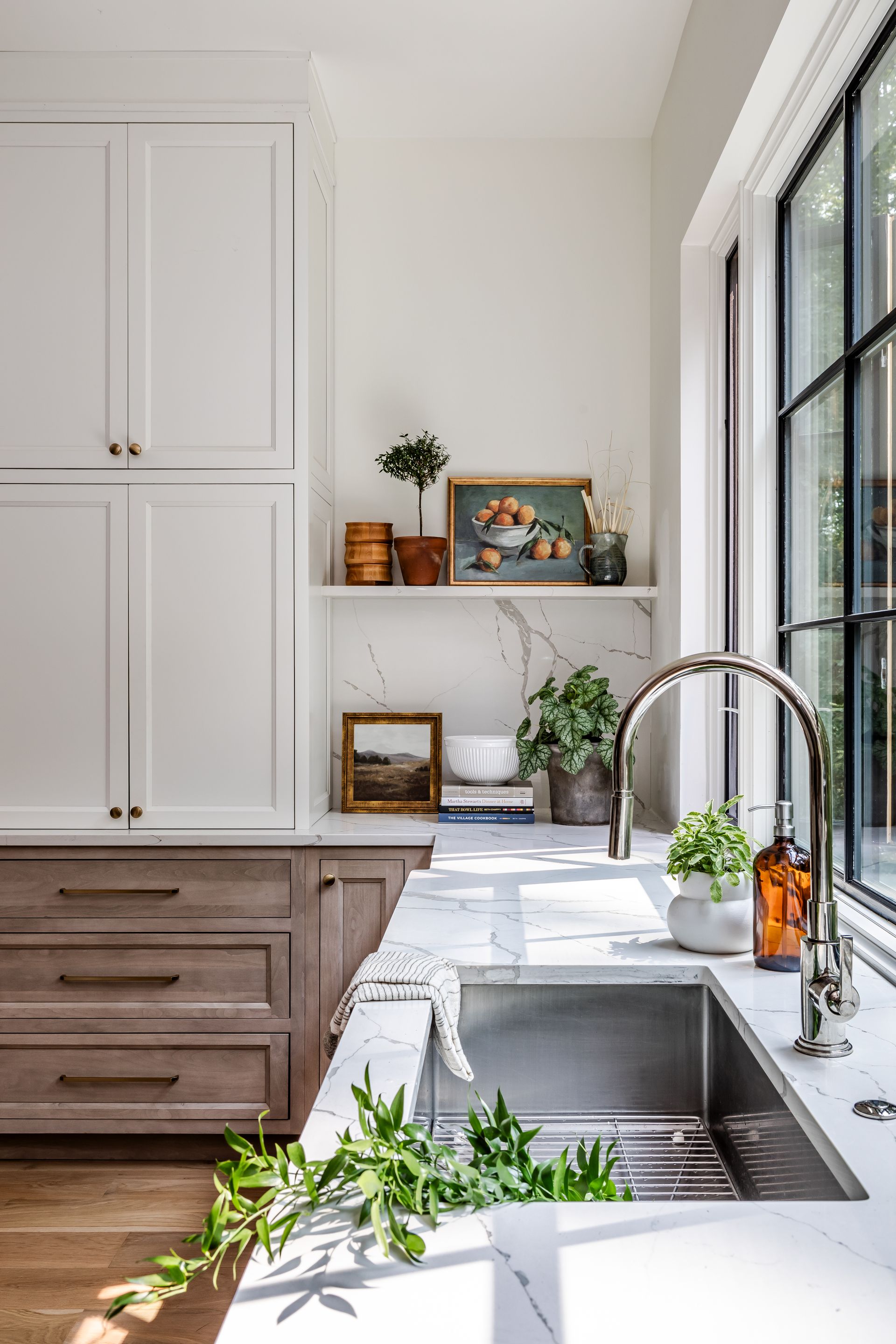 Kitchen with white and wood cabinets, stainless steel sink, plants, and a window.