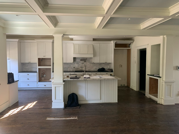 Kitchen interior with white cabinets, island, and ceiling beams; dark hardwood floor.