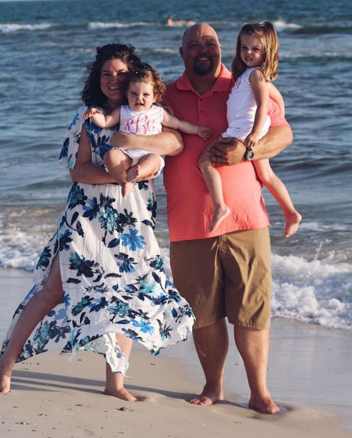 Family on beach; woman holding toddler, man holding child. Ocean in background.