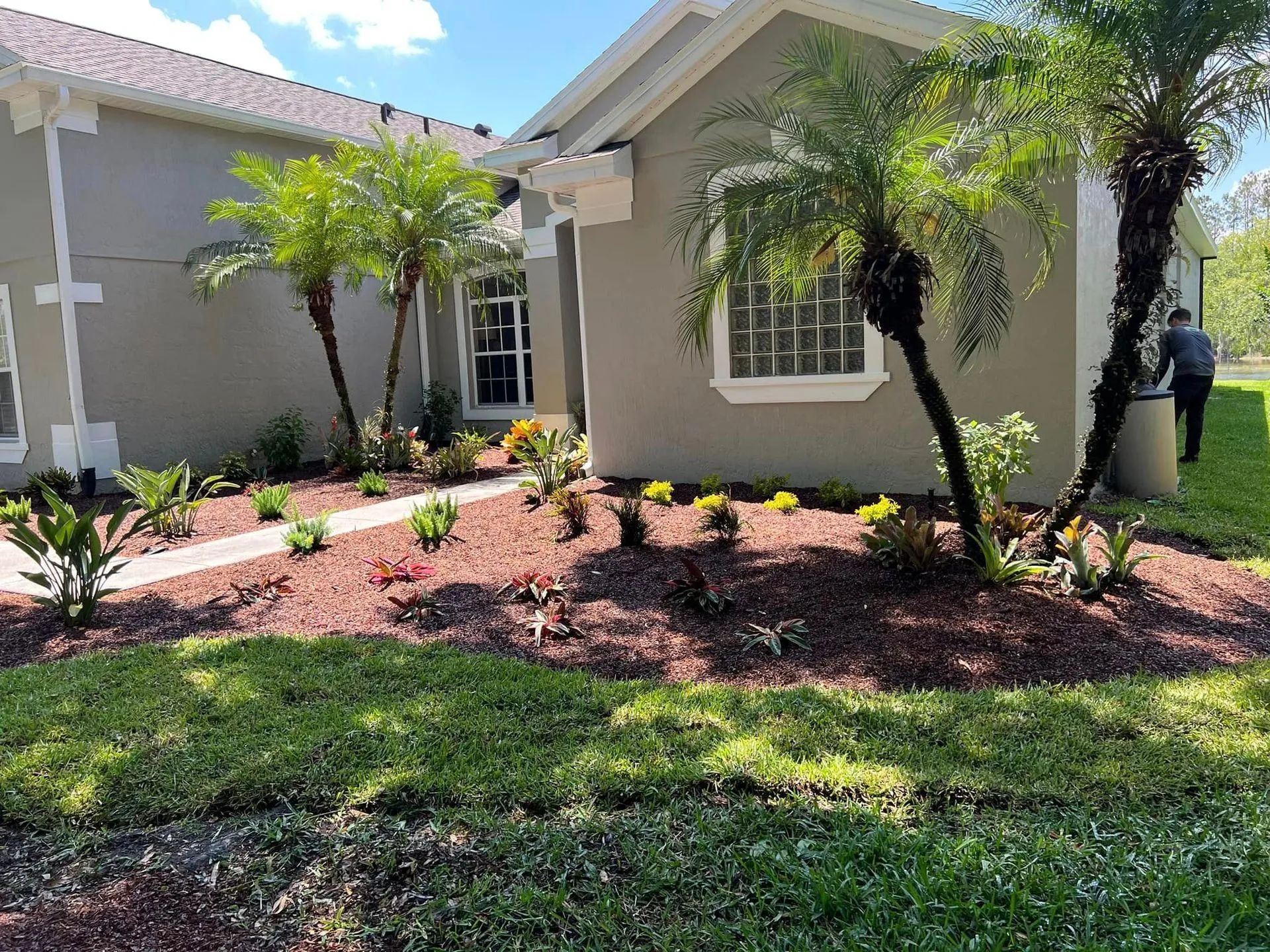 House exterior with palm trees, landscaping, and red mulch beds along a walkway.