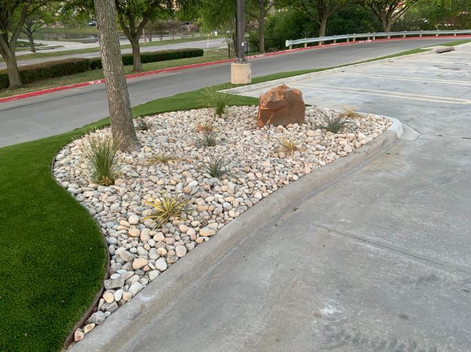 A finished landscape island in a parking lot is decorated with stonework and drought-resistant plants. 