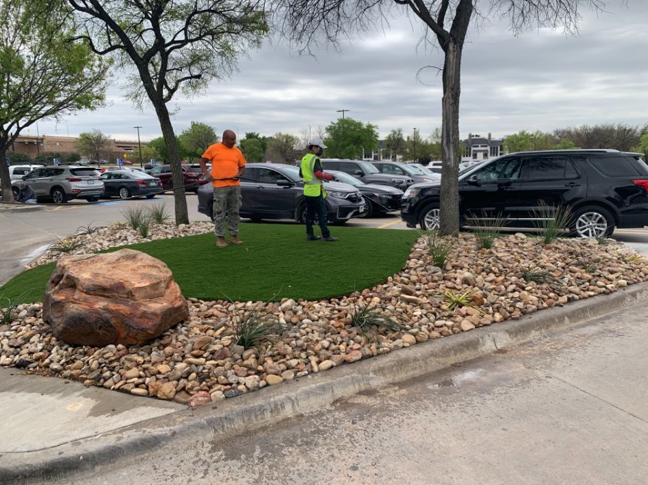 Two men are standing on top of a lush green lawn in a parking lot.