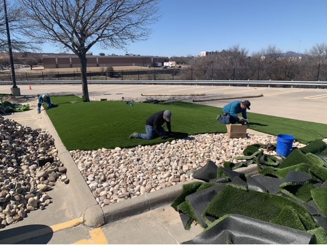 Two men are installing artificial grass in a parking lot