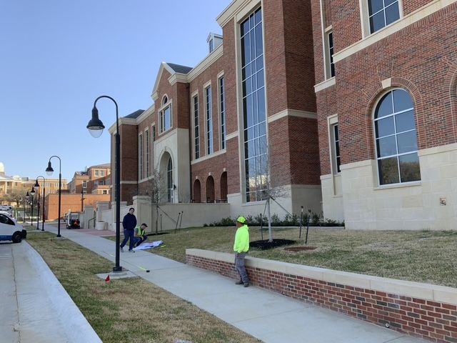 A man in a yellow hard hat is standing in front of a large brick building