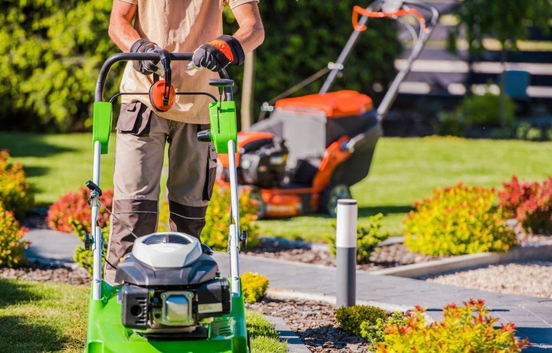 A man is using a green lawn mower to cut the grass in a garden.