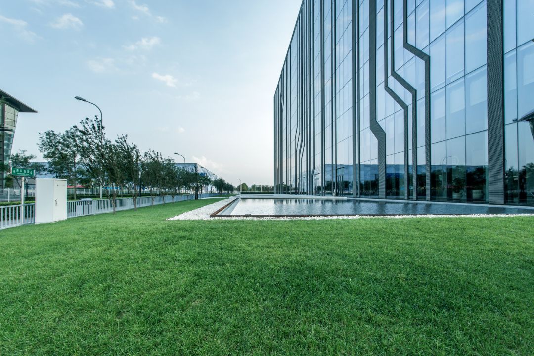 A large building with a lot of windows and a lush green lawn in front of it.