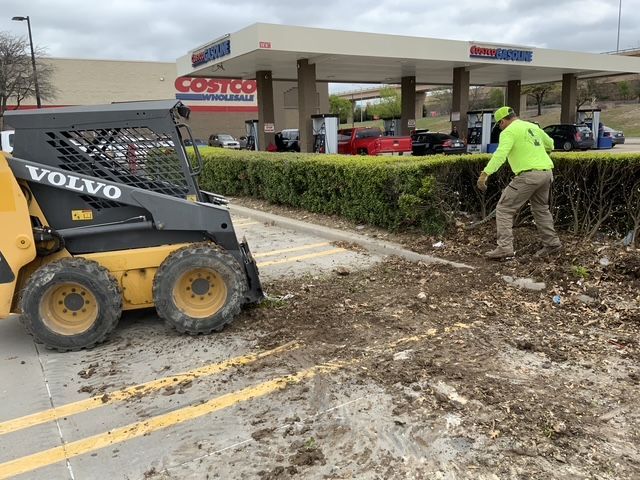 A man is standing next to a volvo skid steer in a parking lot.