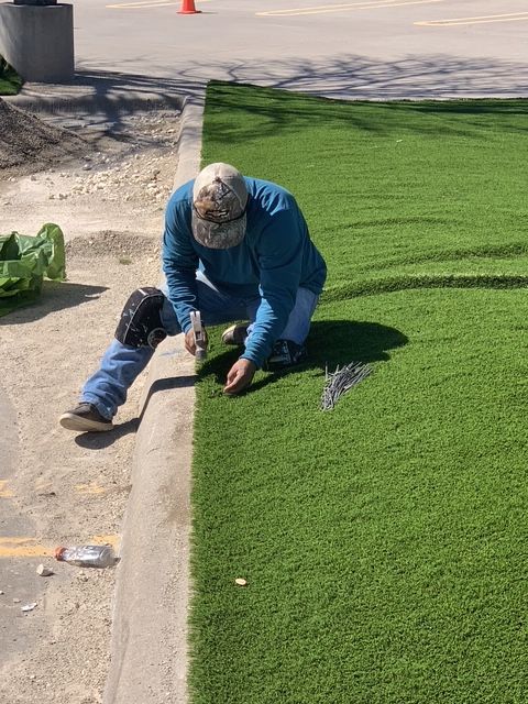 A crew member from 1st Impression Turf is tacking down 