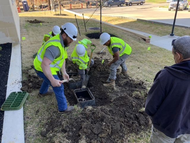 1st Impression Turf crew are working in safety vests and hard hats around junction boxes in the ground. 