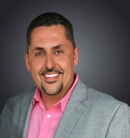 A man in a suit and pink shirt is smiling for the camera.