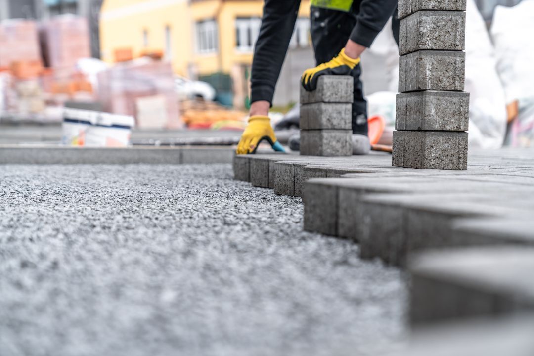 A man is laying bricks on a sidewalk.