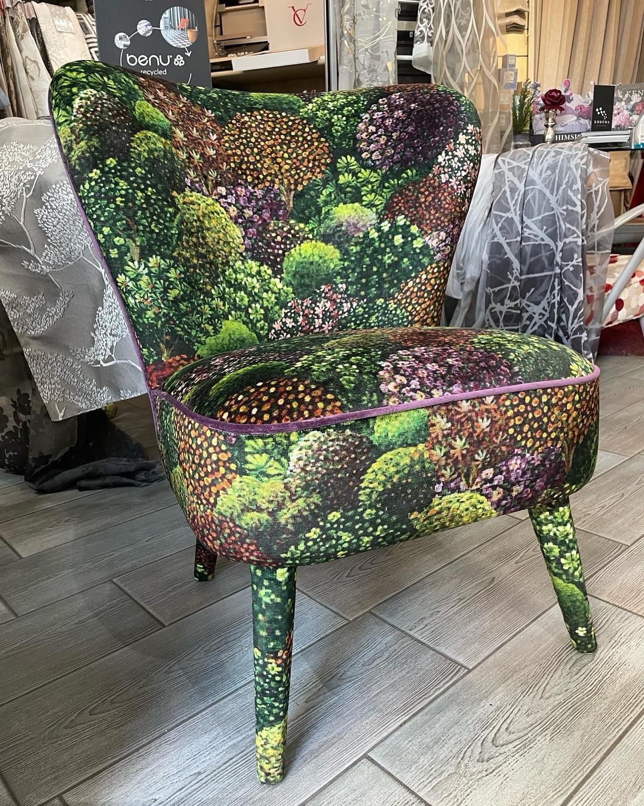 Stanza con carta da parati floreale, pannelli in legno, camino con piastrelle verdi e zona salotto integrata con cuscini.