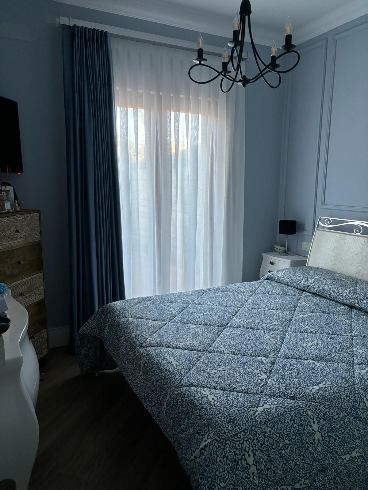 TV montata su una parete ricoperta di carta da parati a motivi geometrici, sopra un mobile in legno. Sul mobile è posizionato un altoparlante bianco.