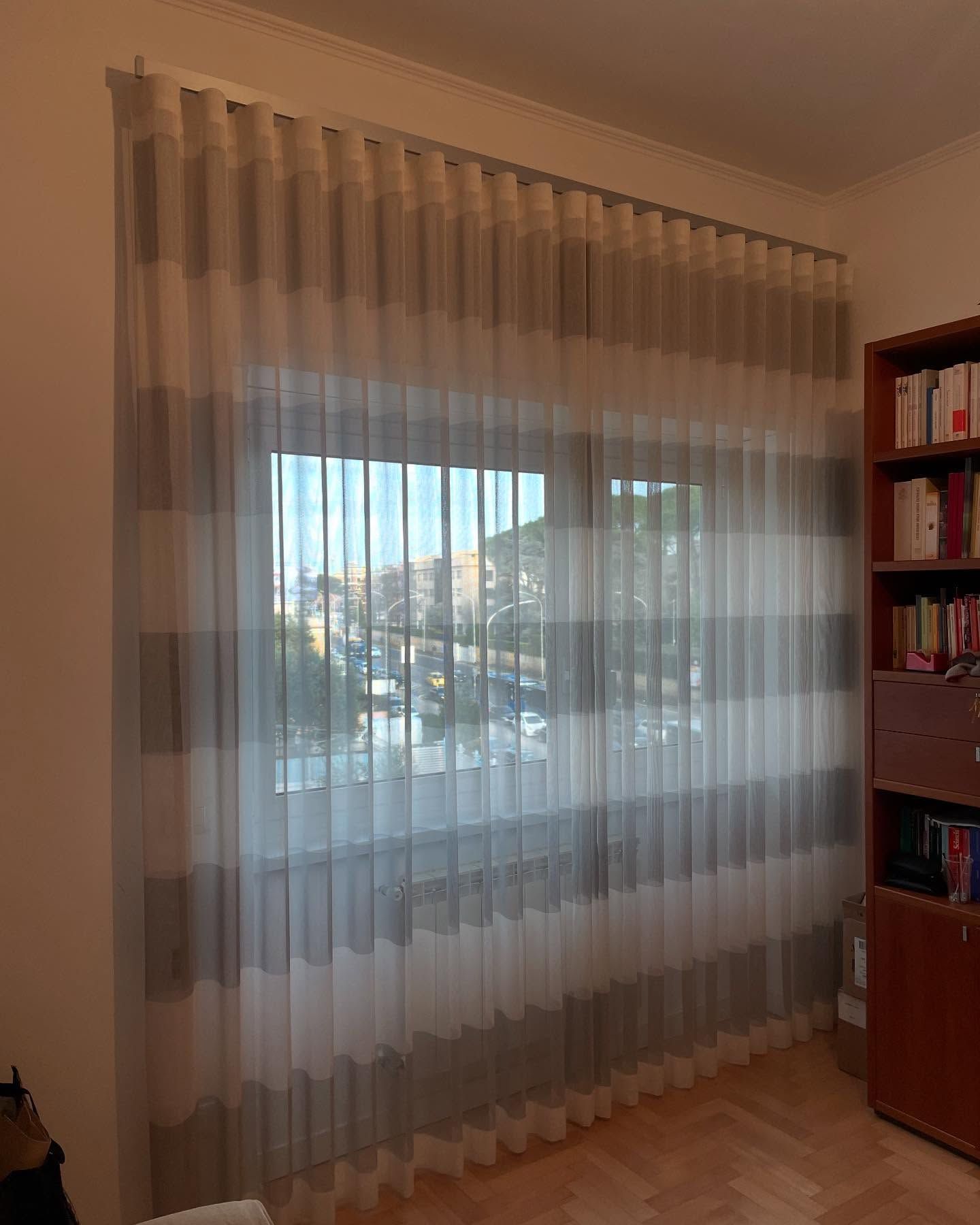 Delle tende trasparenti con strisce grigie sono appese sopra una finestra