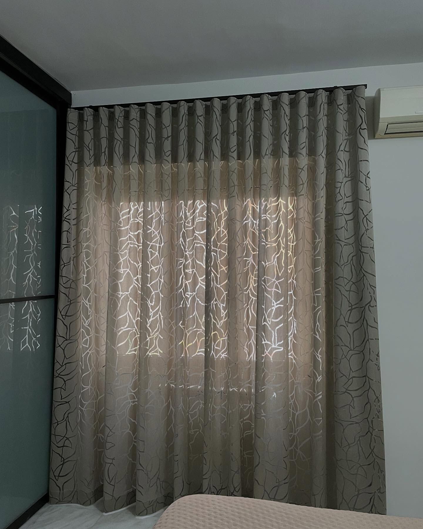 Tende trasparenti con motivi color cuoio appese davanti a una finestra, con un bastone scuro